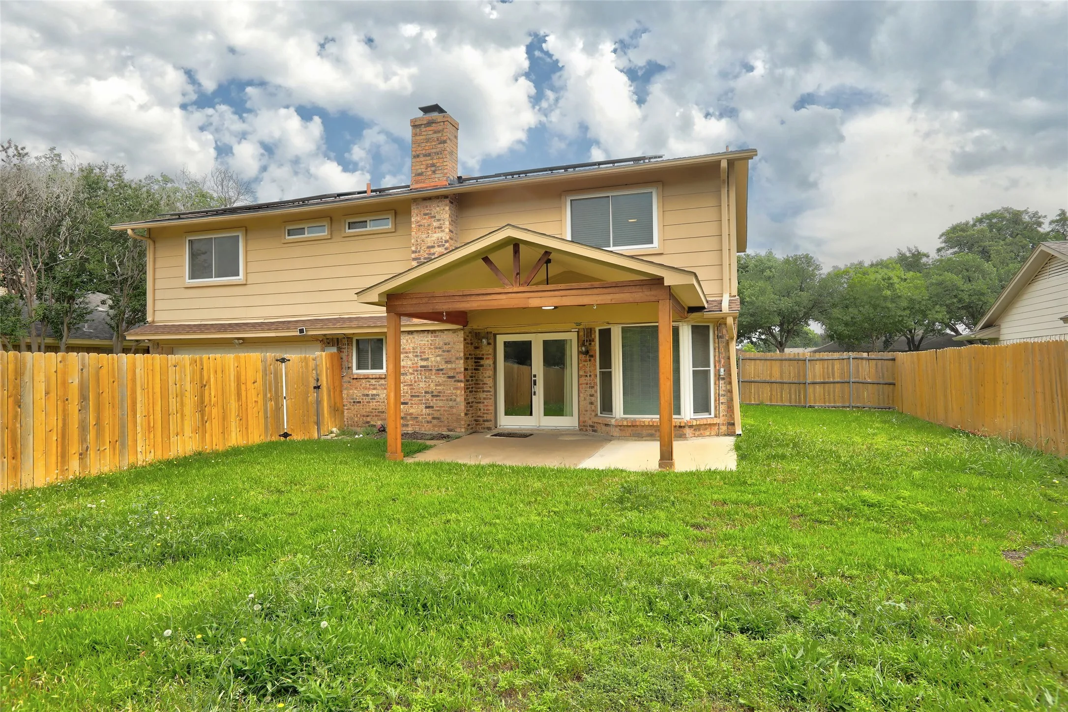 Expansive backyard featuring a covered patio with wood beam accents, a full privacy fence, and a brick exterior with a prominent chimney