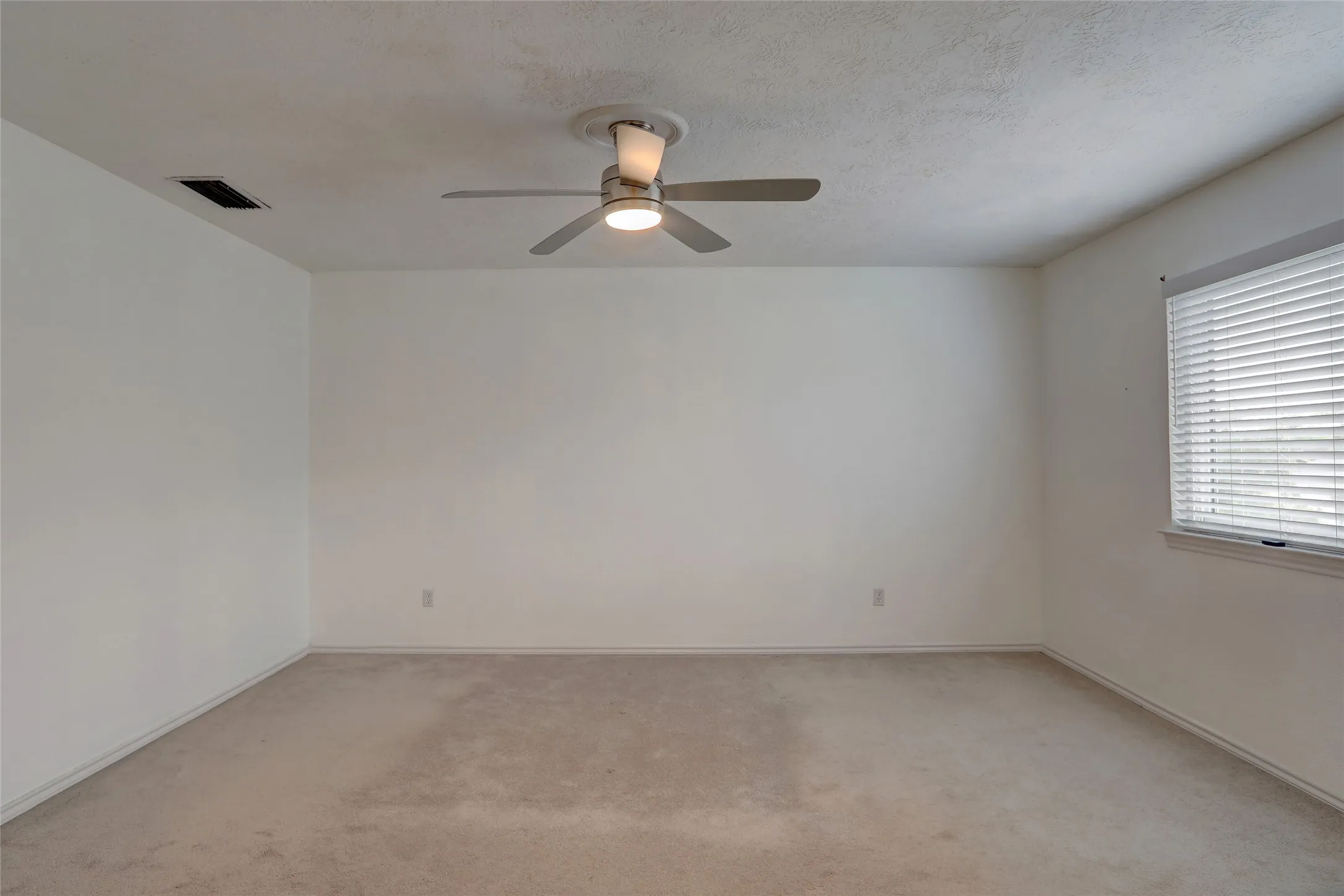 Carpeted room featuring a ceiling fan with integrated lighting, a single window with horizontal blinds, and neutral painted walls