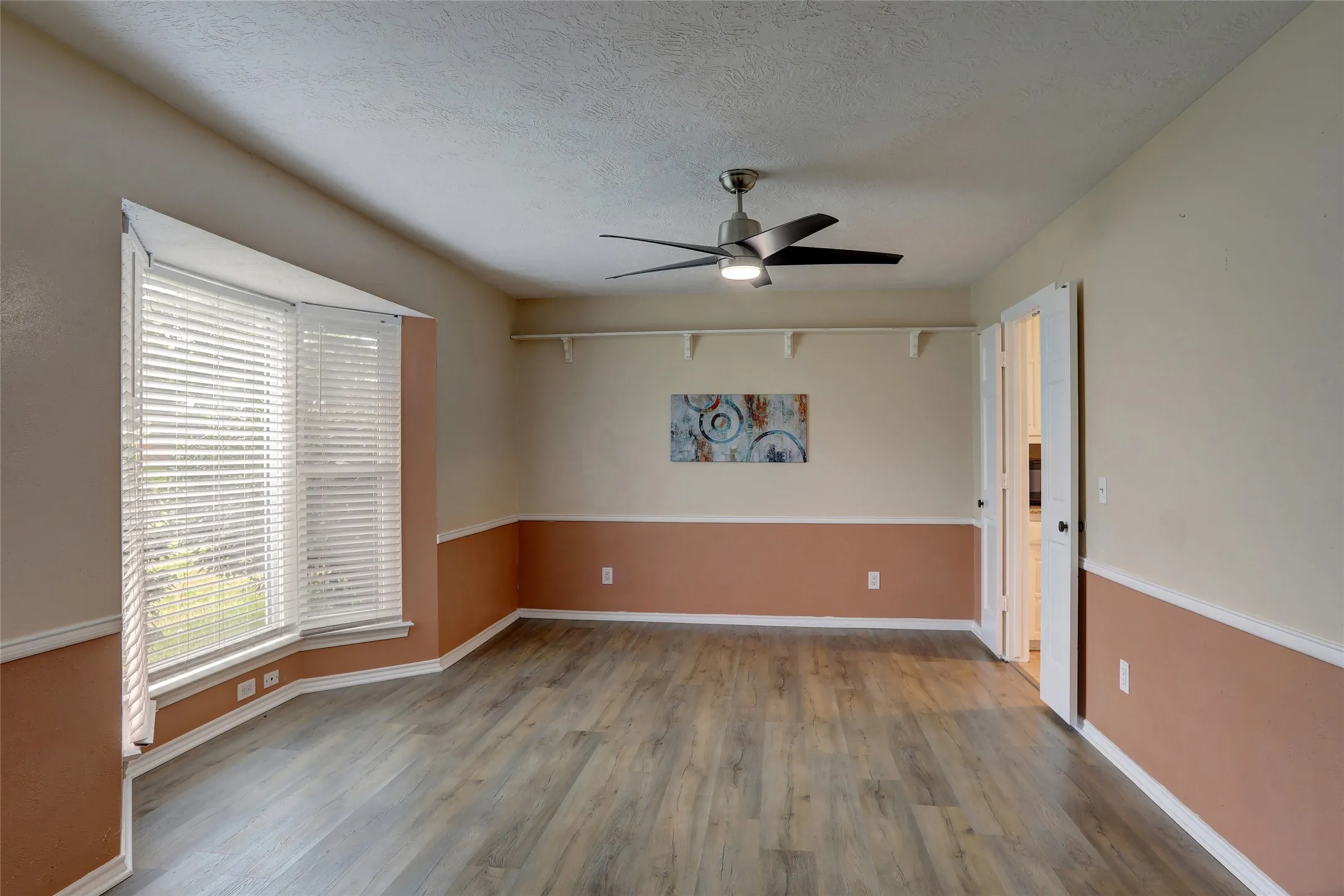 Spacious room featuring wood-finish flooring, a bay window with blinds, and a contemporary ceiling fan
