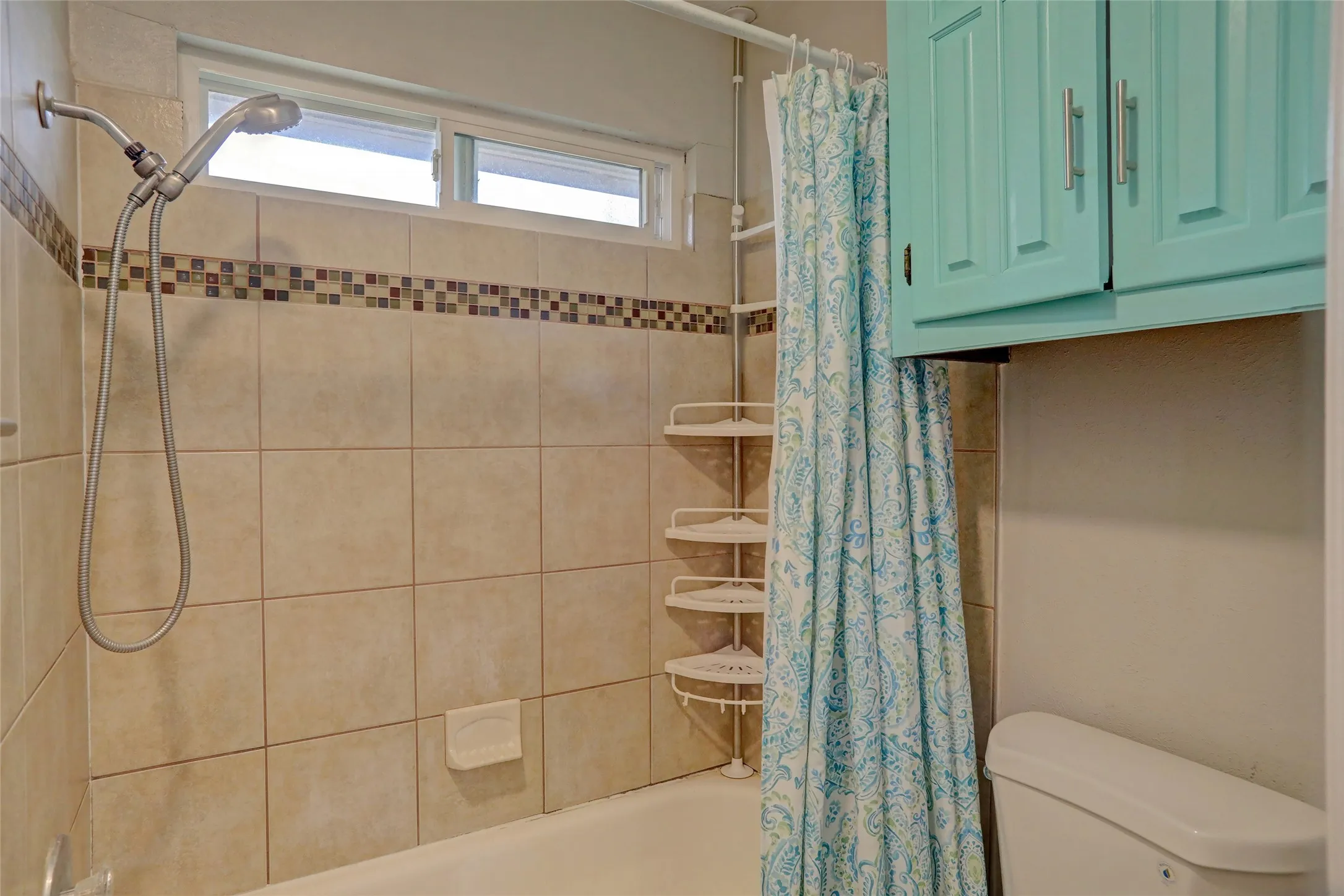 Bathtub shower combination with tan tile surround, mosaic accent band, and a multi-setting showerhead