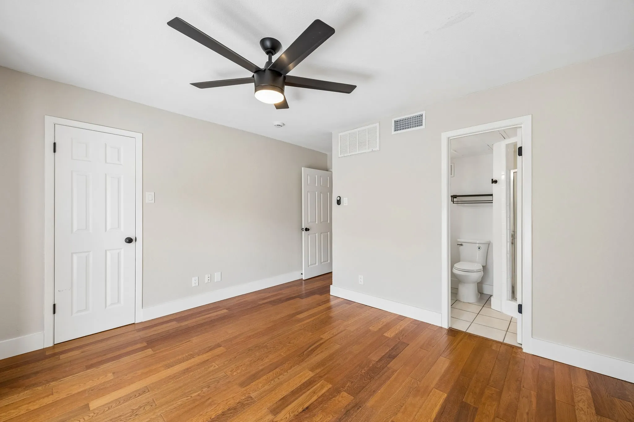 Spacious room featuring wood-finish flooring, light neutral wall paint, and a modern ceiling fan with integrated lighting