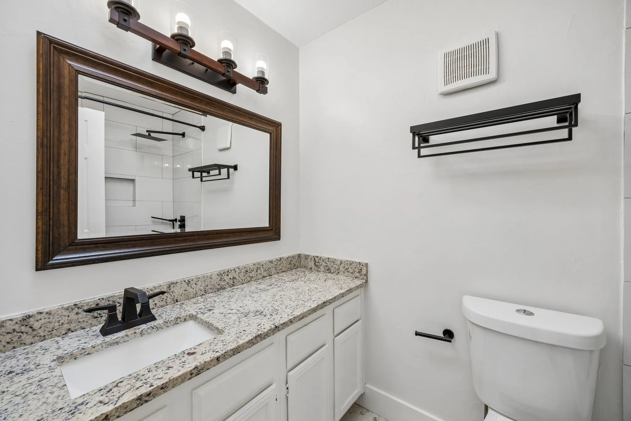 Bathroom vanity featuring a speckled countertop, white cabinetry, a rectangular undermount sink, and a black two-handle faucet