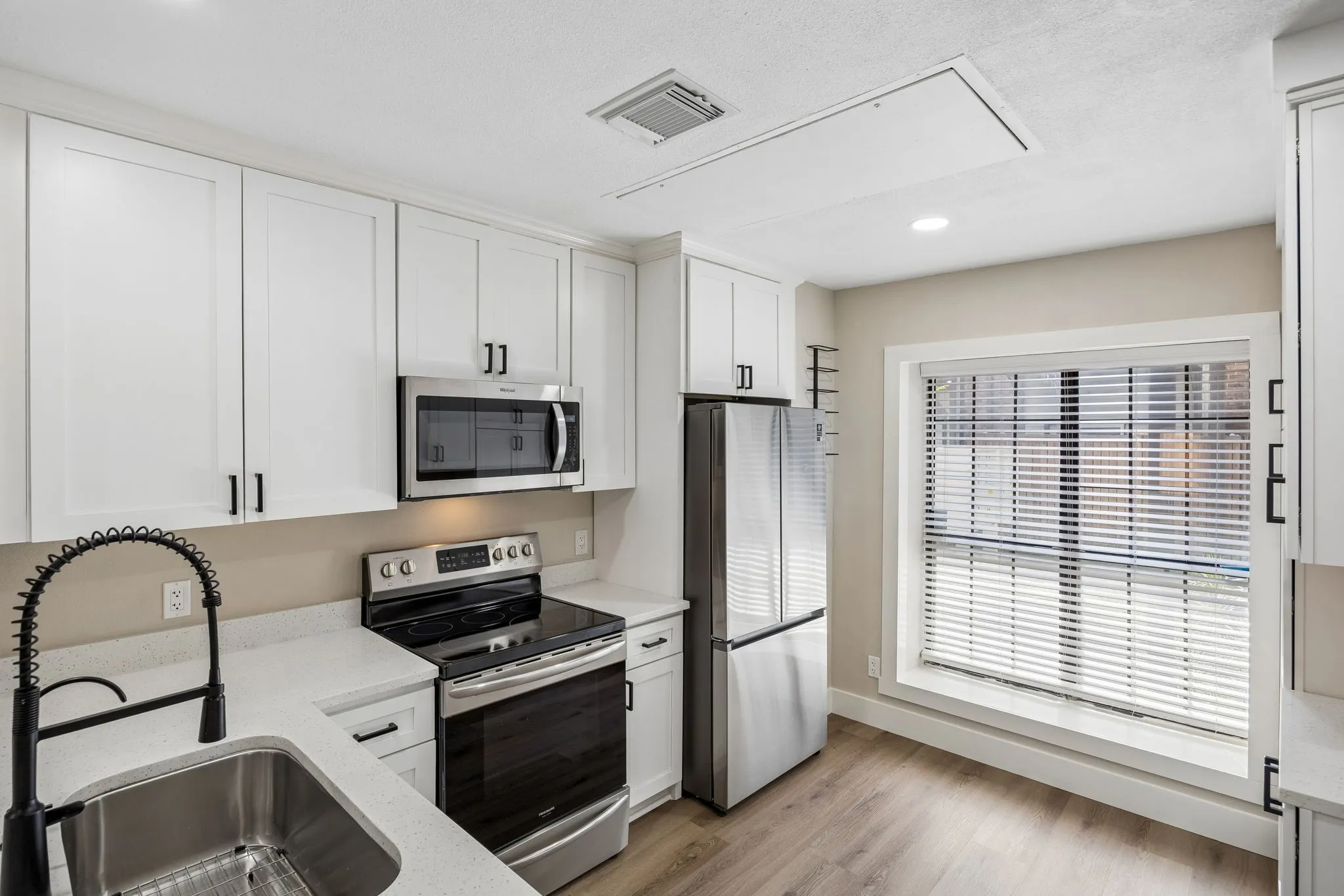 Modern kitchen featuring white shaker cabinetry, stainless steel appliances, light-toned countertops, and wood-finish​​‌​​​​‌​​‌‌​‌‌​​​‌‌​‌​‌​‌​​​‌​​ flooring