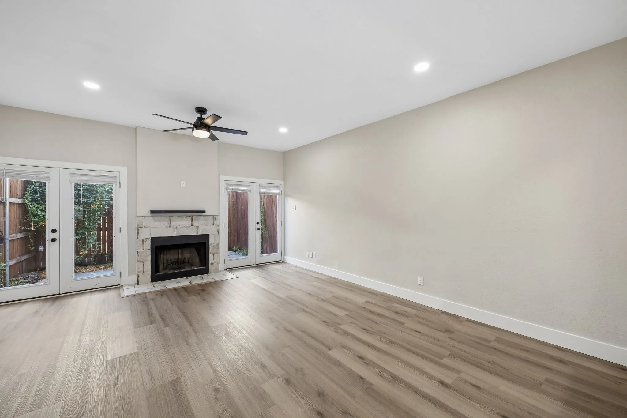 Spacious living area featuring wood-finish flooring, a contemporary fireplace with a stone surround, and multiple glass-paneled French doors