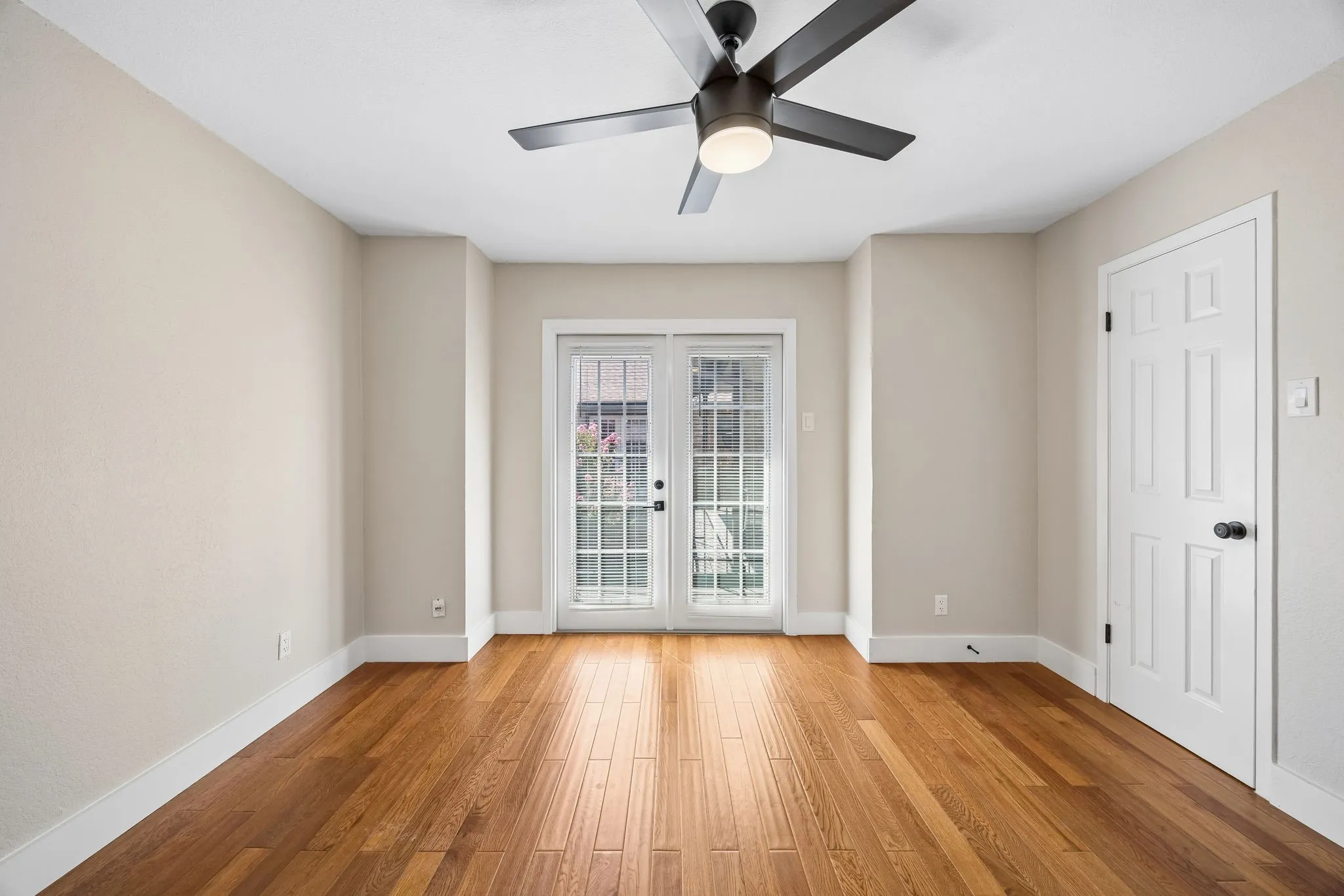 Room featuring wood-finish flooring, neutral wall tones, a contemporary ceiling fan with integrated lighting, and white trim throughout