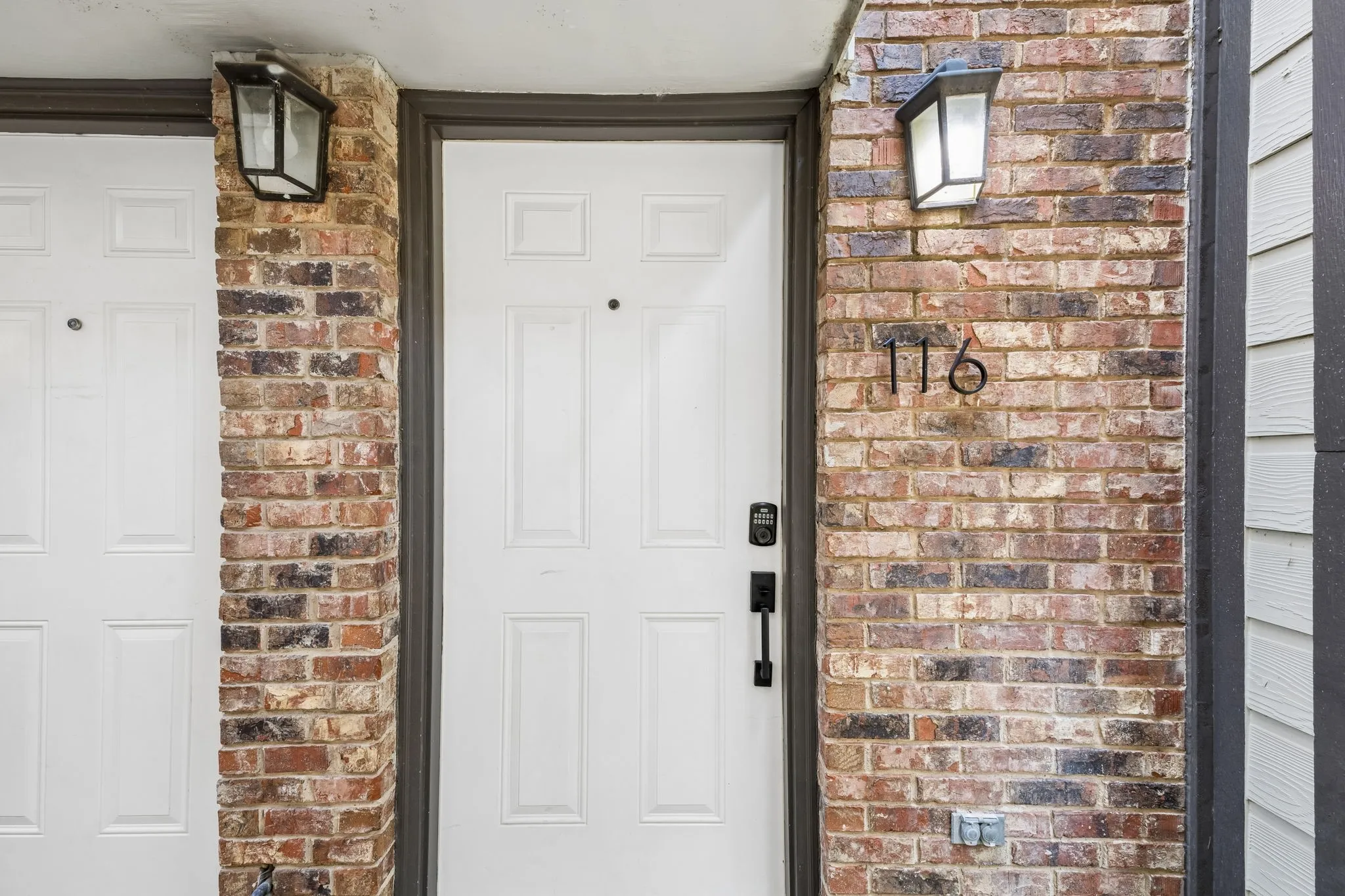 Exterior entry featuring a white paneled door with black hardware, flanked by a brick column