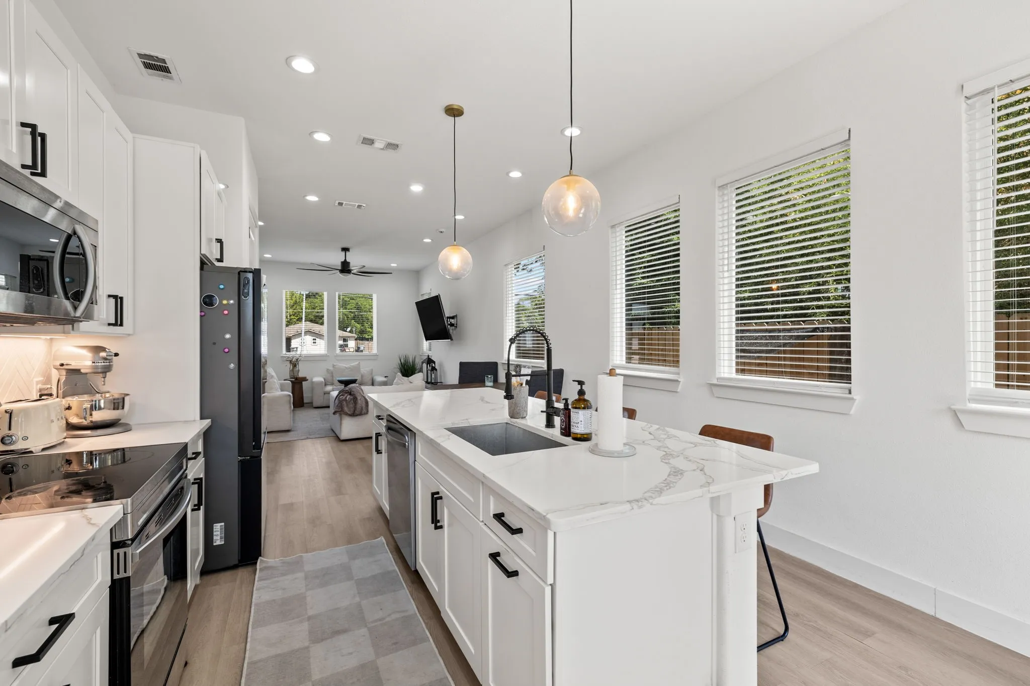 Modern kitchen featuring white cabinetry, integrated stainless steel appliances, a center island with sink and seating, and wood-finish flooring
