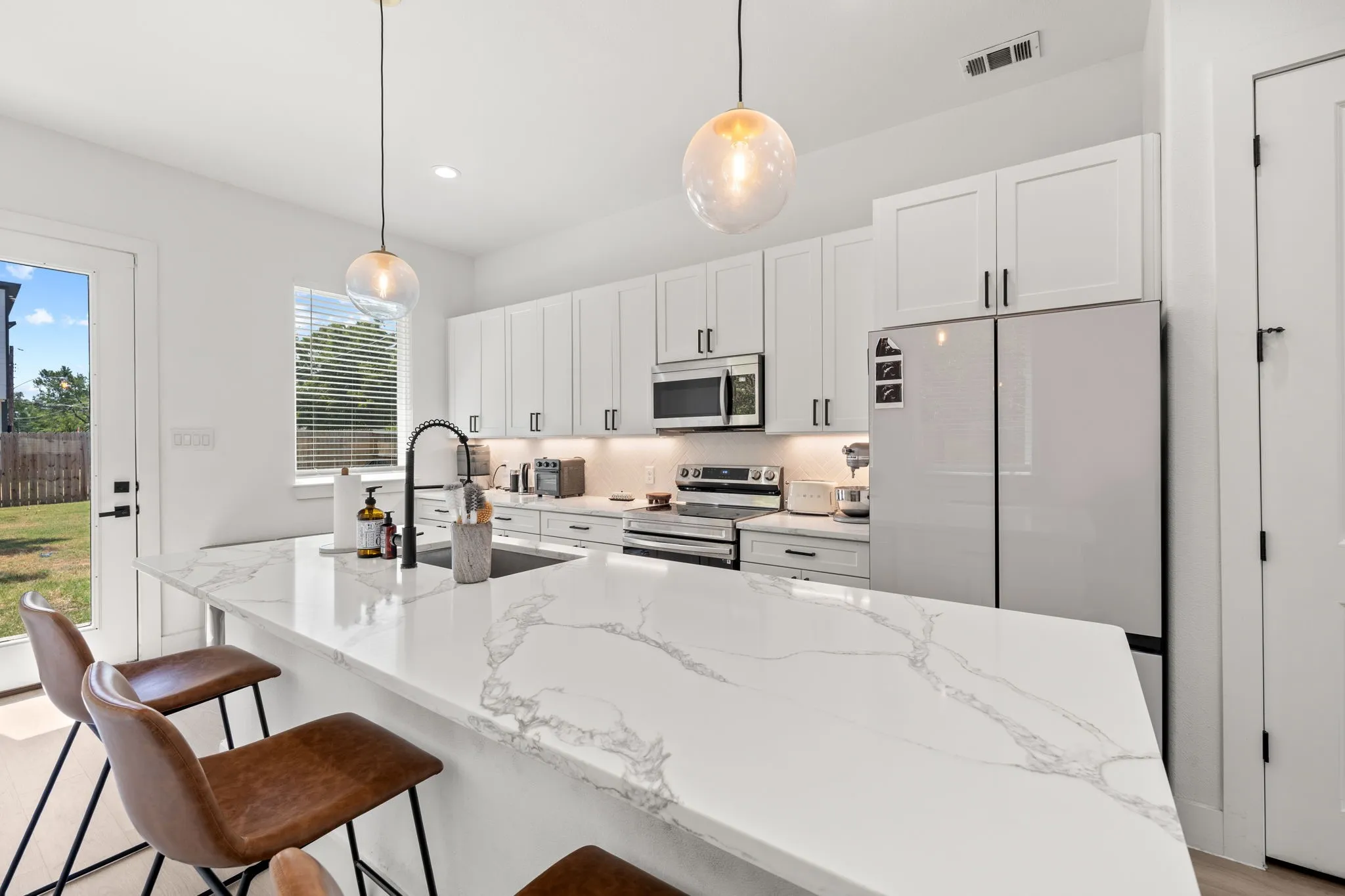 Gourmet kitchen featuring a large island with a waterfall countertop, contemporary white cabinetry, stainless steel appliances, and sleek pendant lighting
