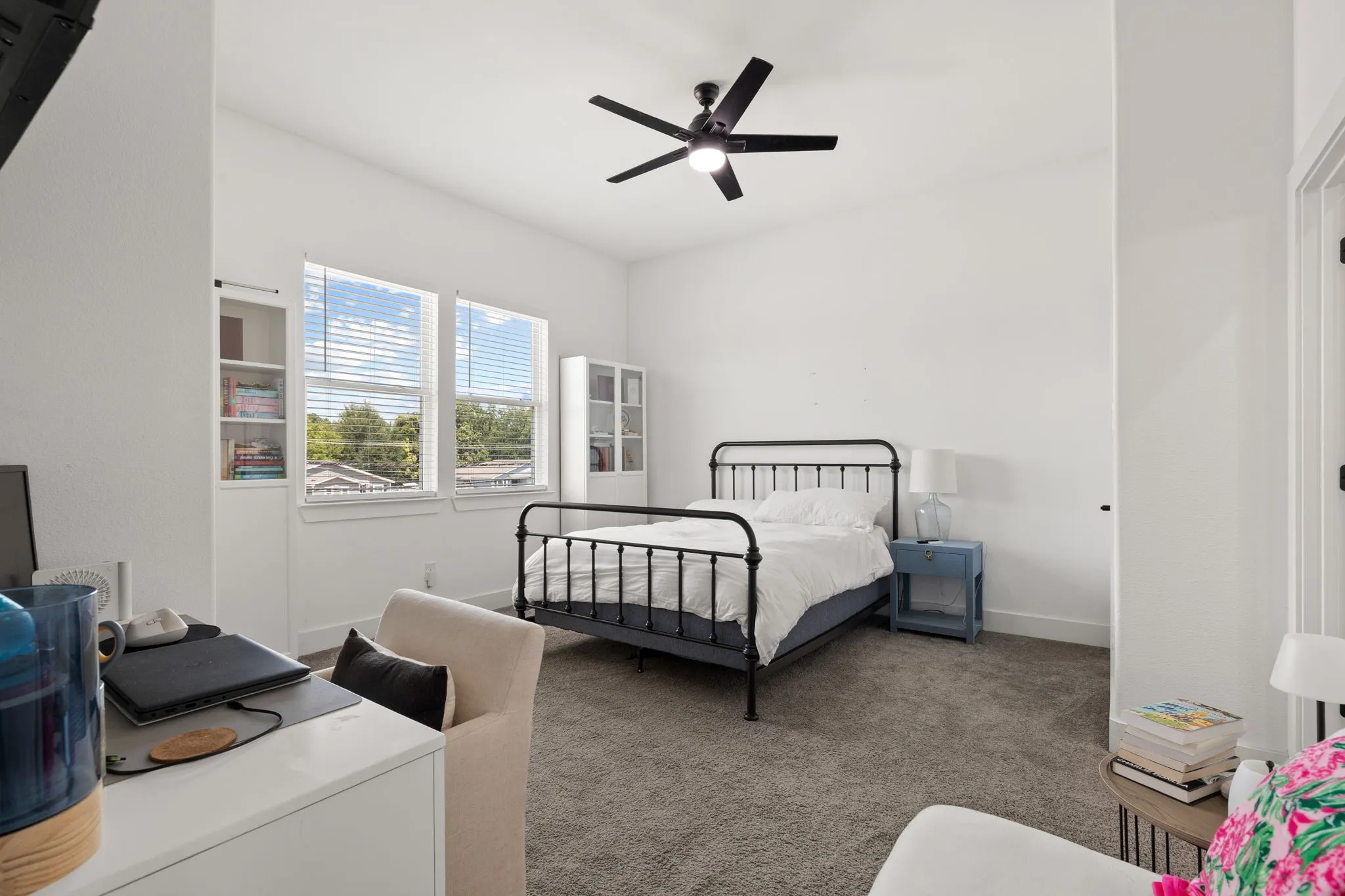 Spacious bedroom with black metal bed frame, carpet flooring, and ceiling fan