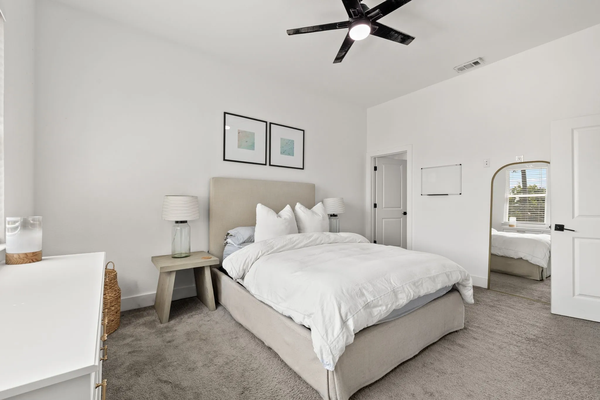 Carpeted room featuring white walls, a black ceiling fan, and a neutral upholstered headboard