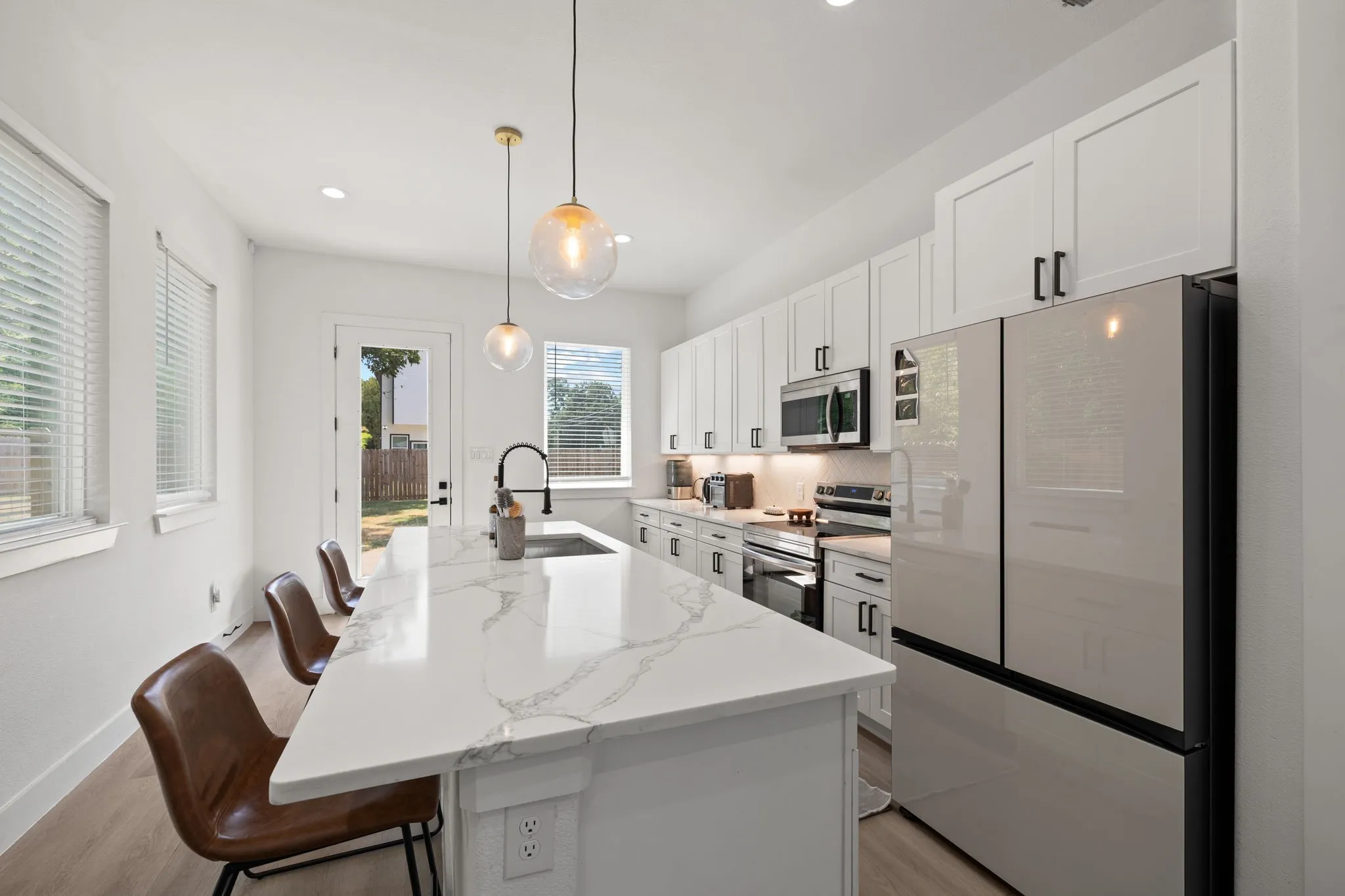 Modern kitchen featuring a large island with a waterfall countertop, white shaker cabinetry, stainless steel appliances, and wood-finish flooring