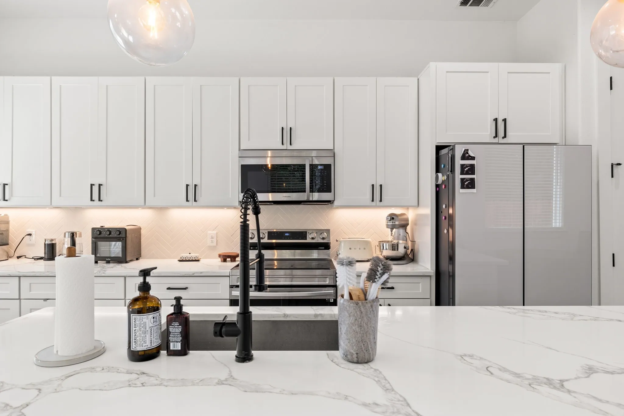 Contemporary white cabinetry with brushed nickel hardware frames this chef's kitchen, anchored by a striking marble-finish waterfall island