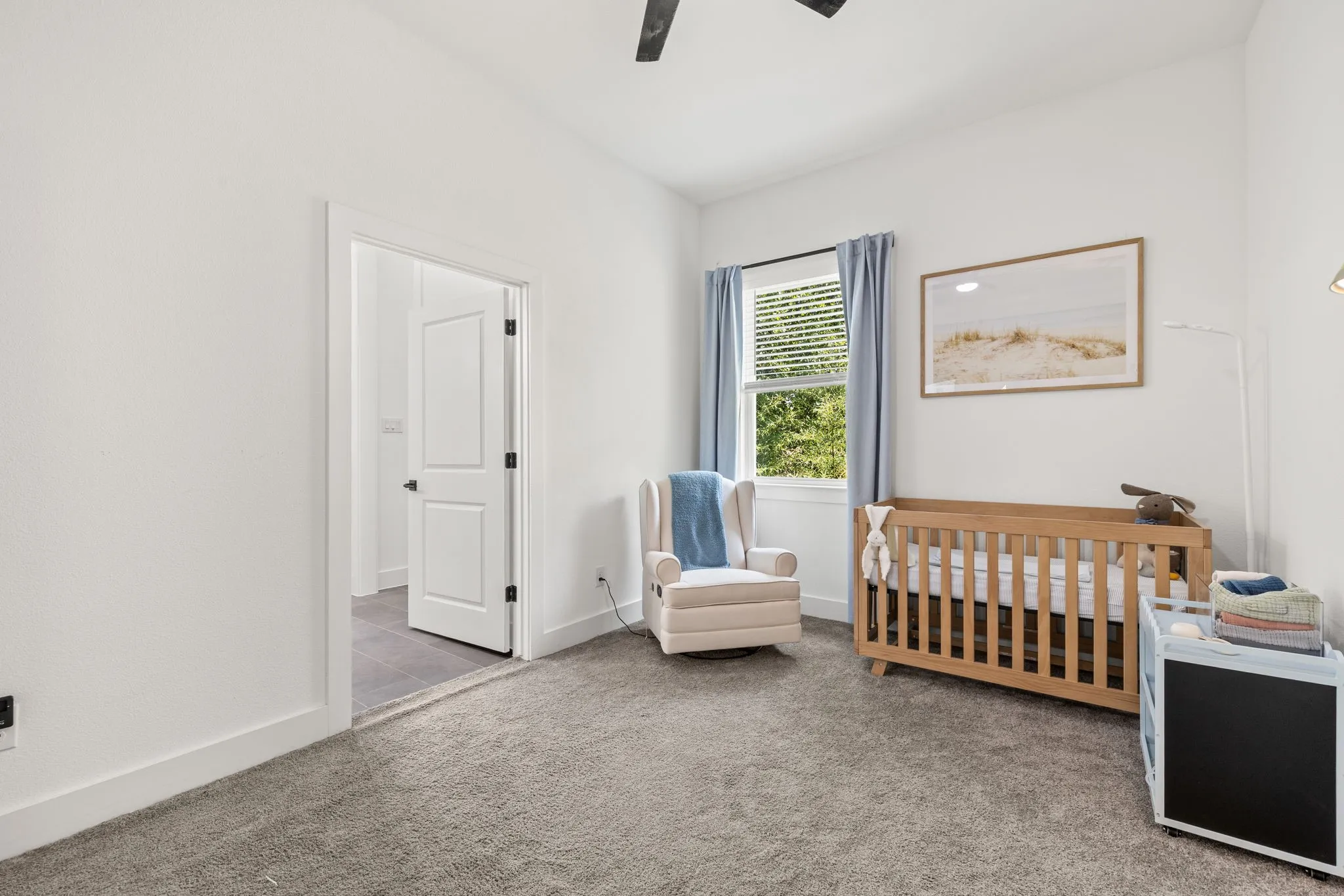 Carpeted room featuring a white interior door, a window with blinds and blue drapes, and a ceiling fan