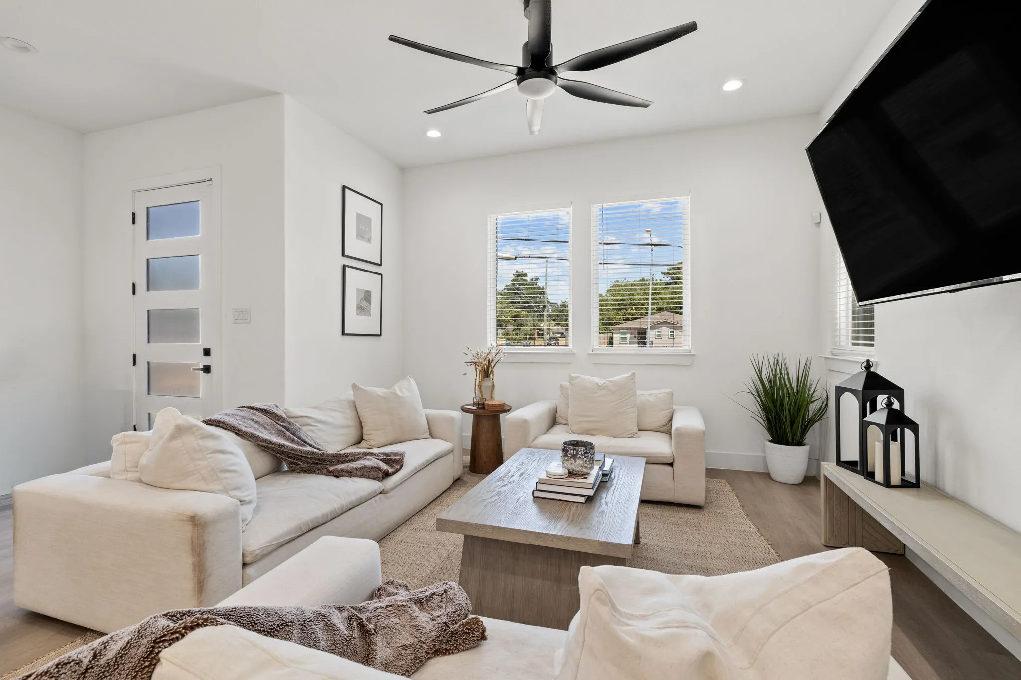 Bright living area featuring wood-finish flooring, white walls, two large windows with blinds, and recessed lighting