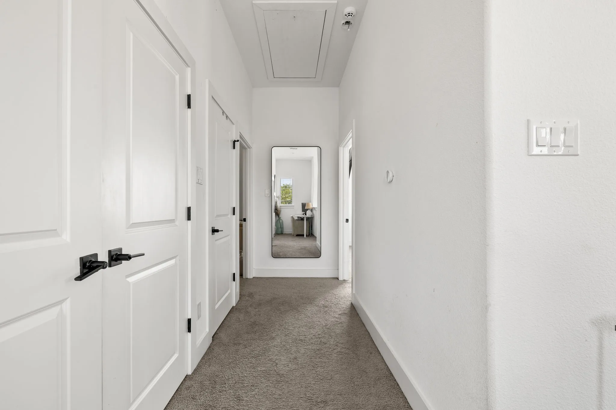 Bright, clean hallway featuring white panel doors, neutral gray flooring, and recessed ceiling lighting