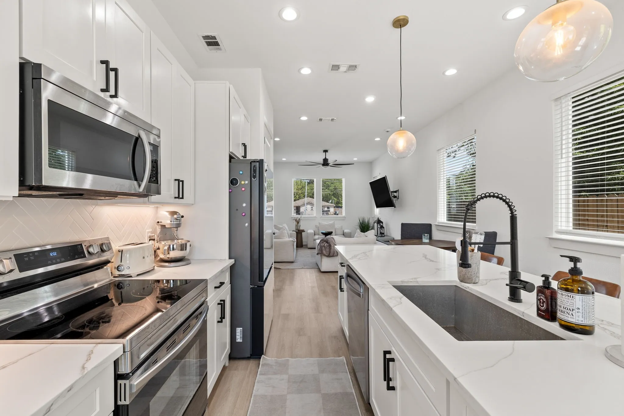 Modern kitchen showcasing white cabinetry with black hardware, stainless steel appliances, light-toned countertops, and a large island with an undermount sink and matte black faucet