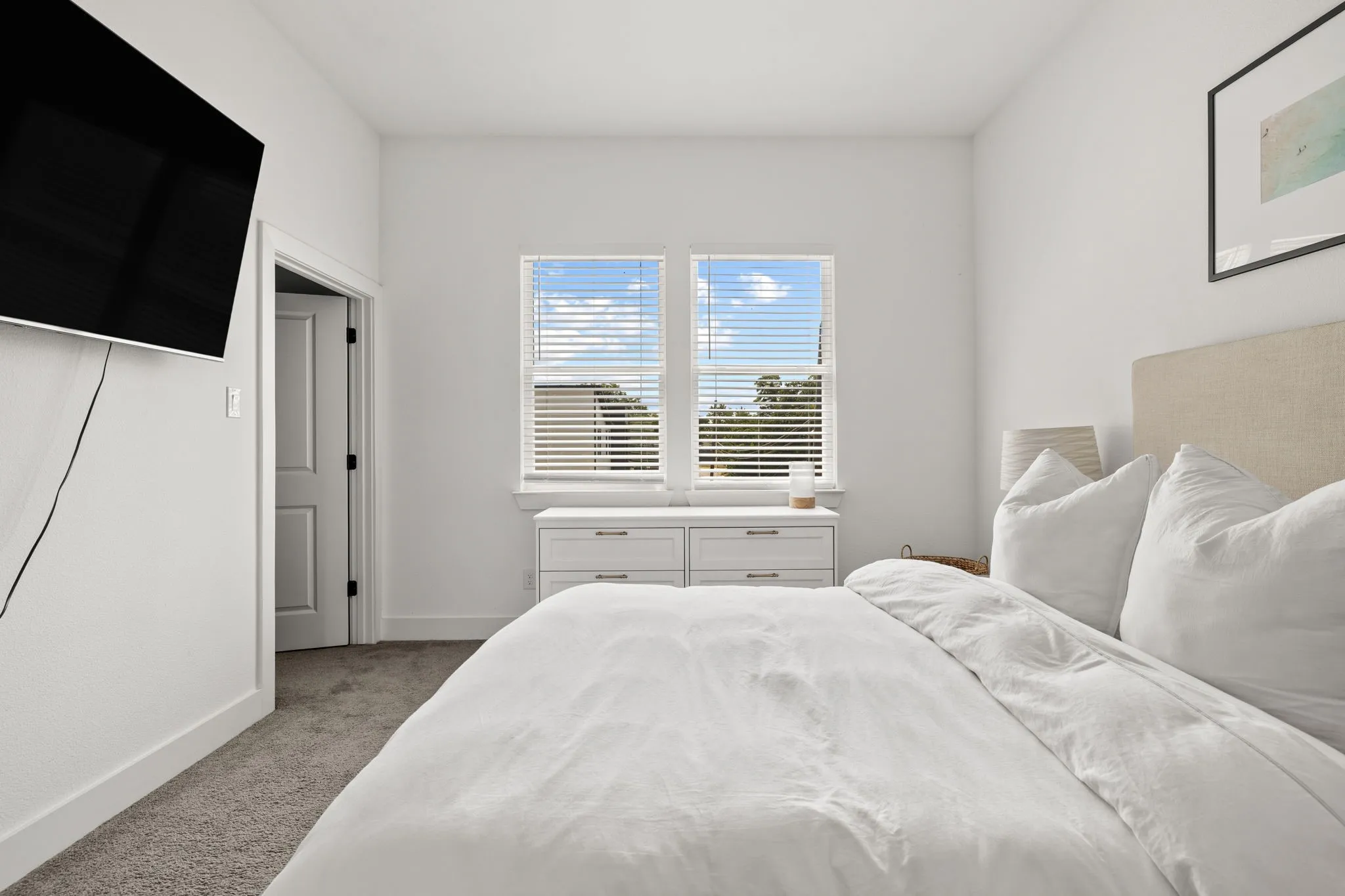 Bright, light-filled bedroom featuring a neutral color palette with crisp white bedding, upholstered headboard, and wood-finish nightstands with integrated drawers