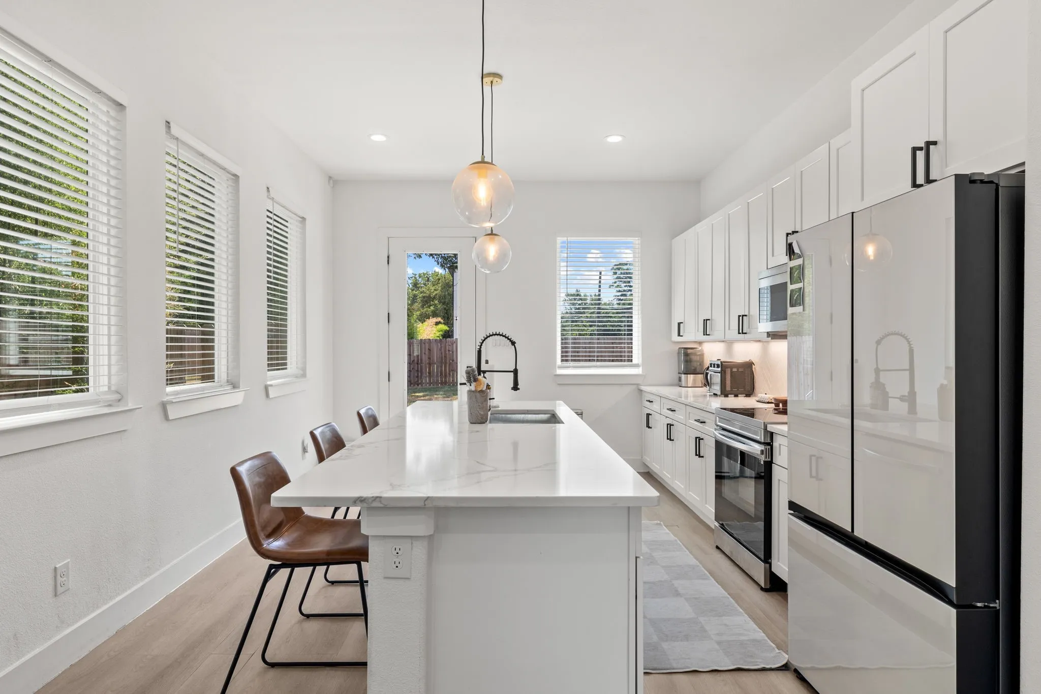 Contemporary kitchen featuring a large central island with a sink, white cabinetry with black hardware, stainless steel appliances, and light wood-finish flooring
