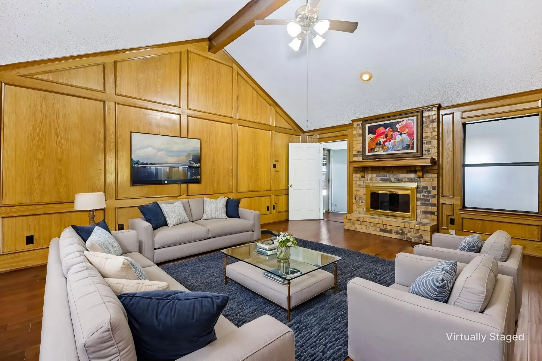 Warm paneling and brick fireplace accented by vaulted beamed ceiling creates a cozy atmosphere in the living room.
