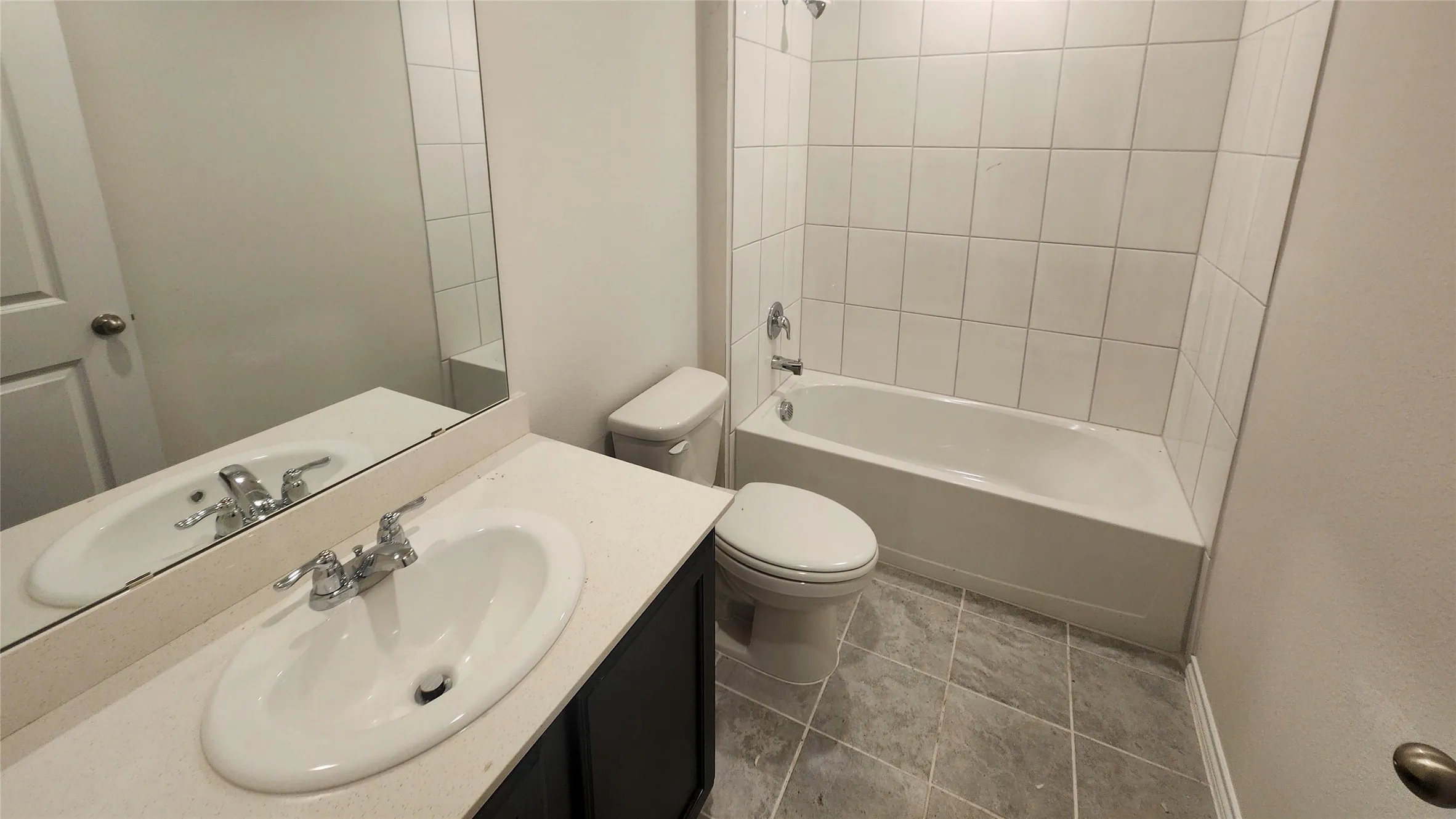 Clean and functional bathroom featuring a round pedestal sink with chrome fixtures, ceramic tile walls, and a tile-surround bathtub with shower combination