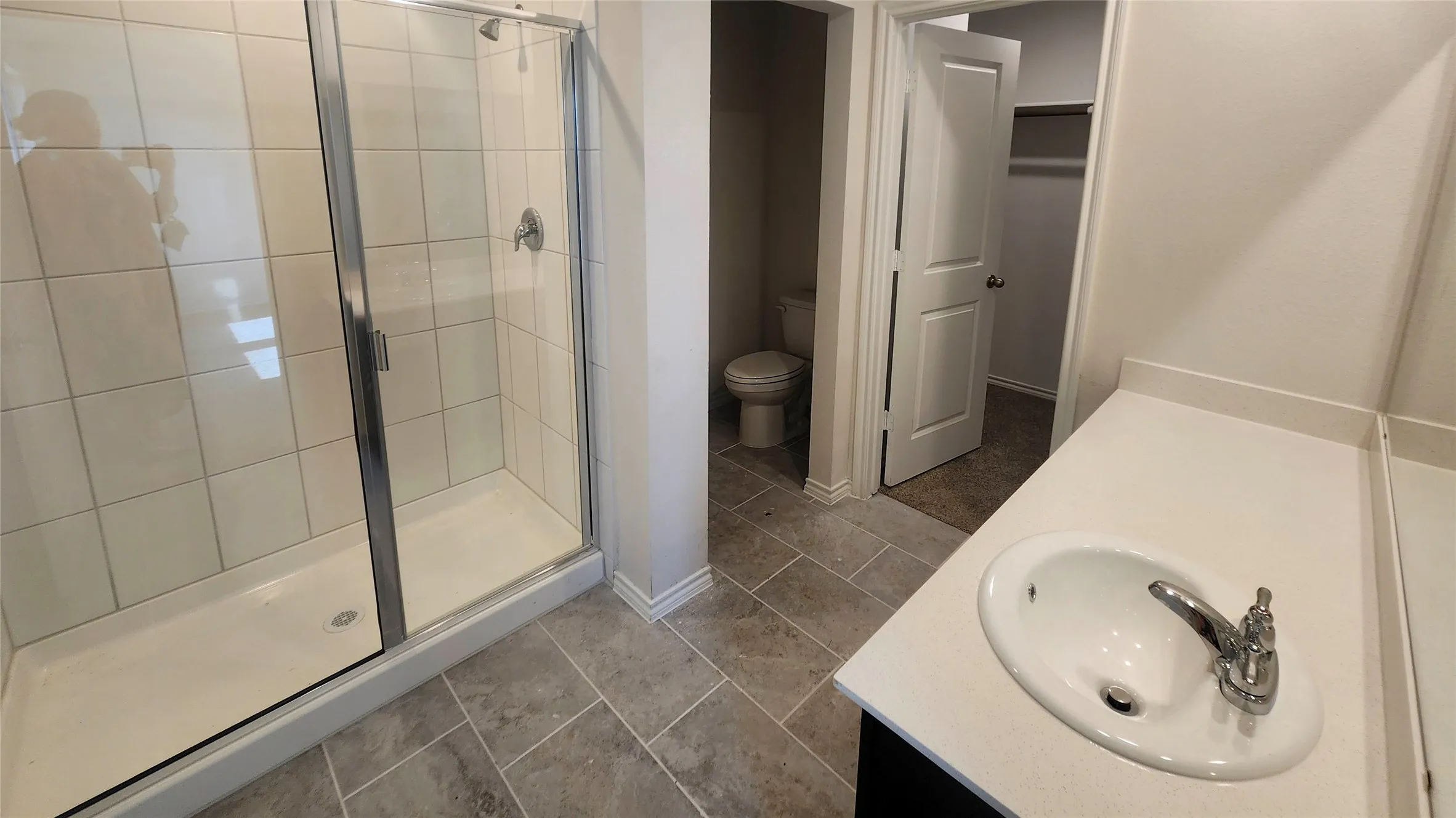 Modern bathroom featuring a sleek vanity with round vessel sink and chrome faucet, ceramic tile shower enclosure with frameless glass door, dark tile flooring throughout, and direct access to a separate toilet room