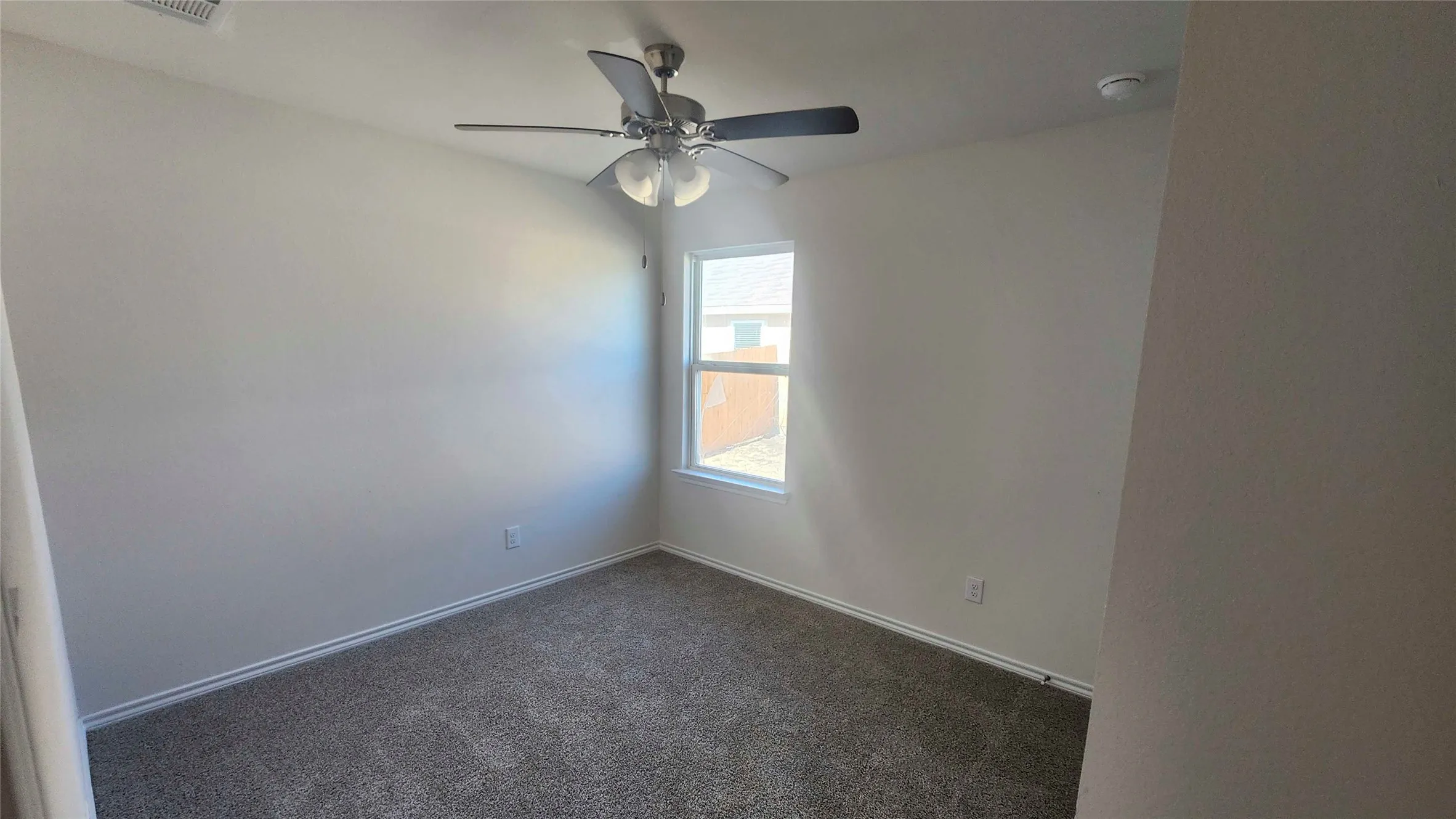 Neutral-toned room with plush carpeting, a single window, a ceiling fan with integrated lighting, and white baseboards