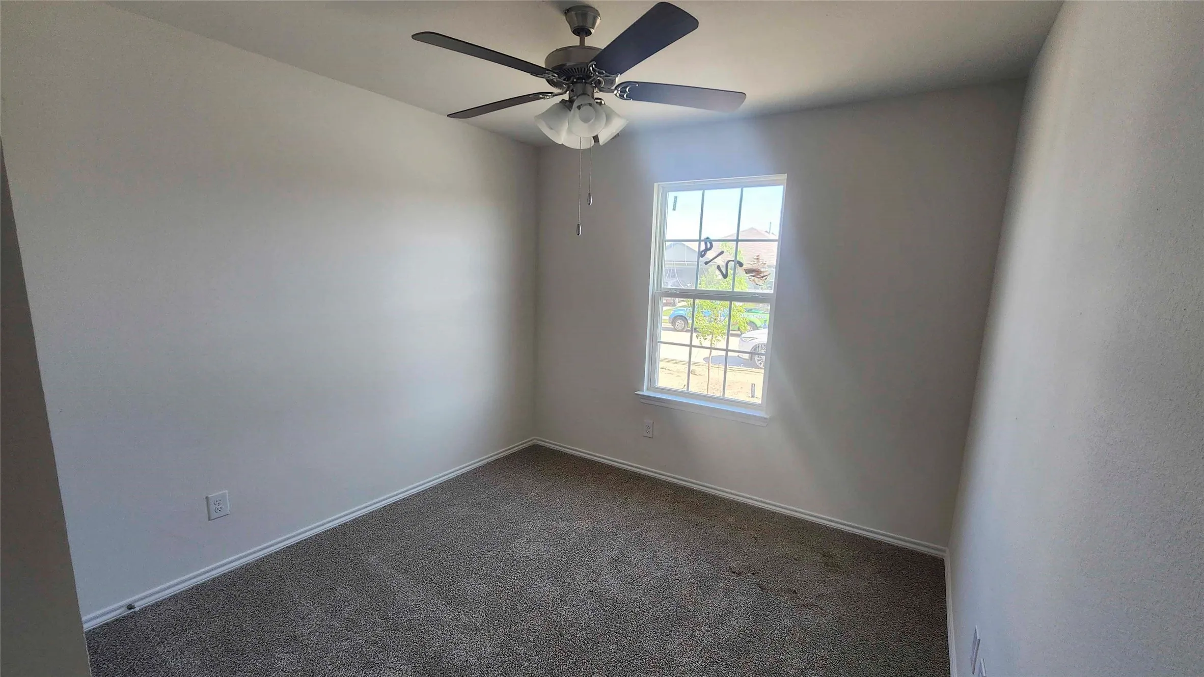 Bright bedroom with neutral carpet flooring, ceiling fan with integrated lighting, and large window providing natural light