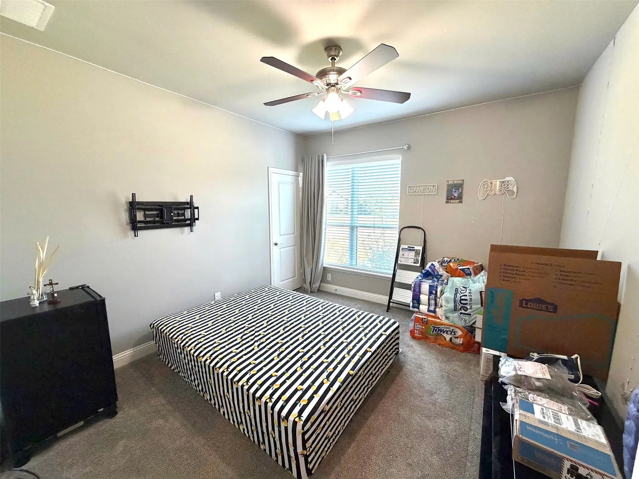 Comfortable secondary bedroom featuring a ceiling fan with integrated lighting, carpeted flooring, and a large window with blinds and curtains providing natural light and privacy
