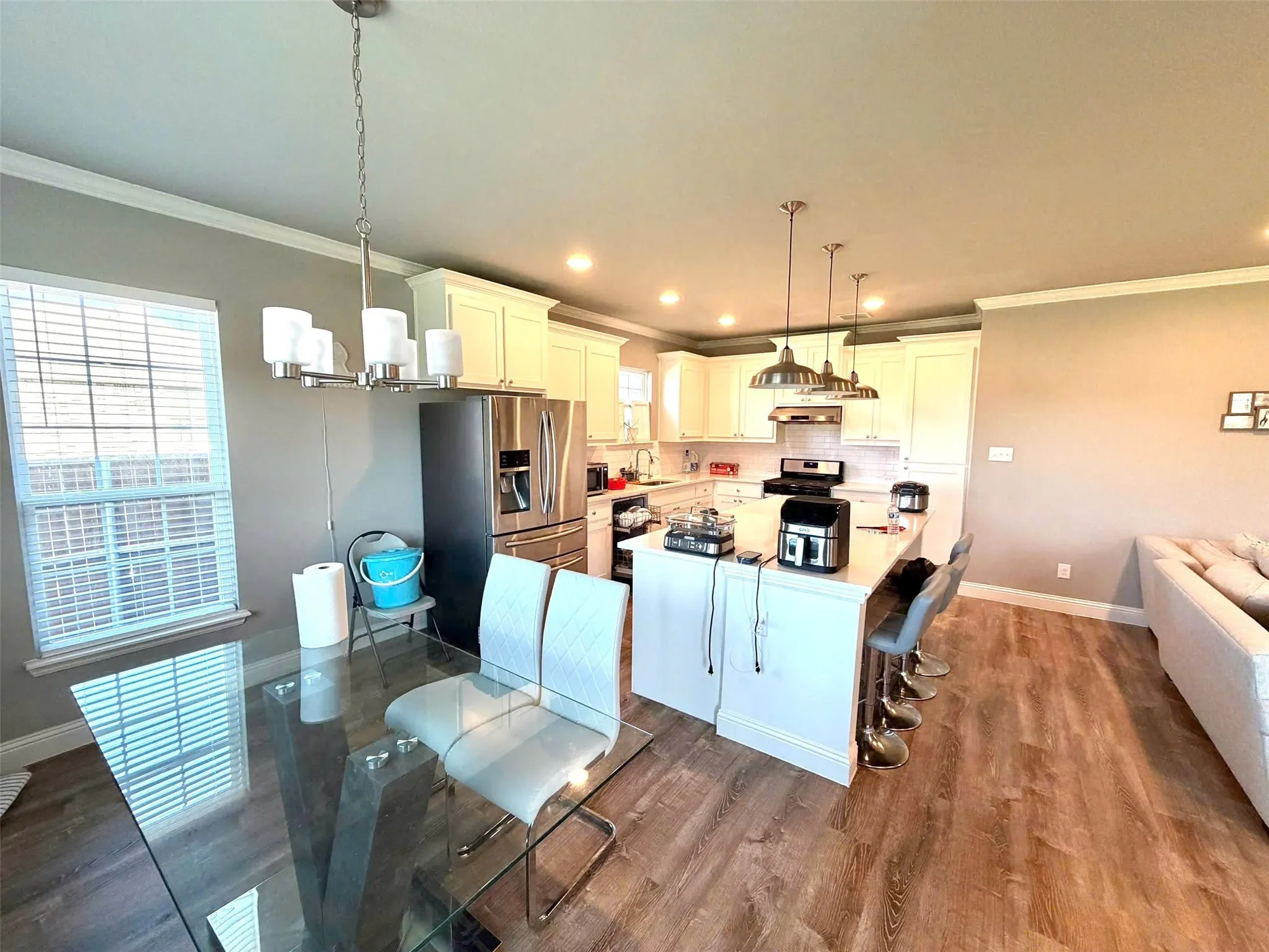 Open-concept kitchen and dining area featuring wood-finish flooring, white cabinetry, a kitchen island with pendant lighting, and stainless steel appliances