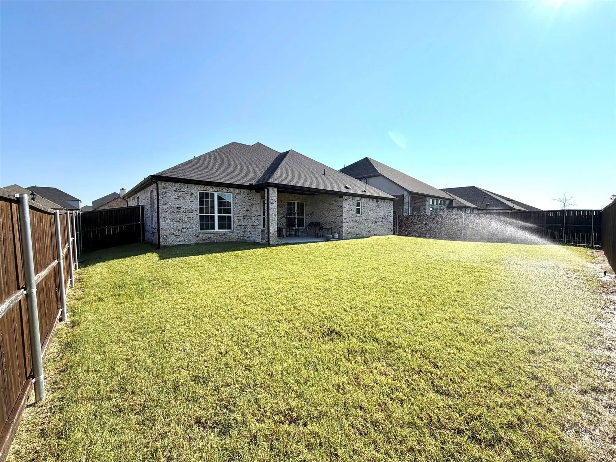 Spacious backyard featuring a large grass lawn, brick exterior, covered patio, and wood privacy fencing