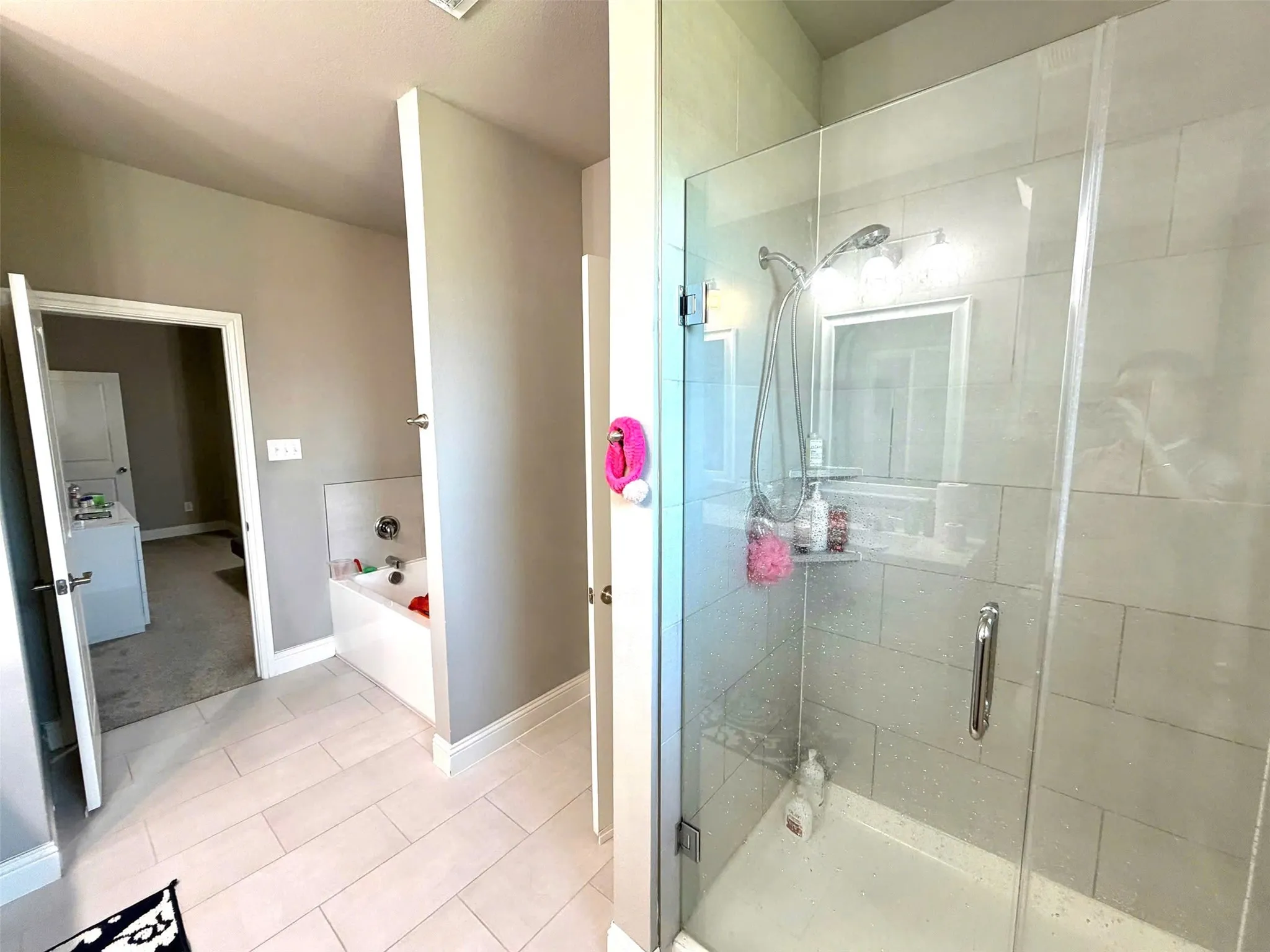 Spa-inspired primary bathroom featuring a frameless glass-enclosed shower with subway tile surround, dual vanity area with integrated lighting, and light-finish tile flooring throughout