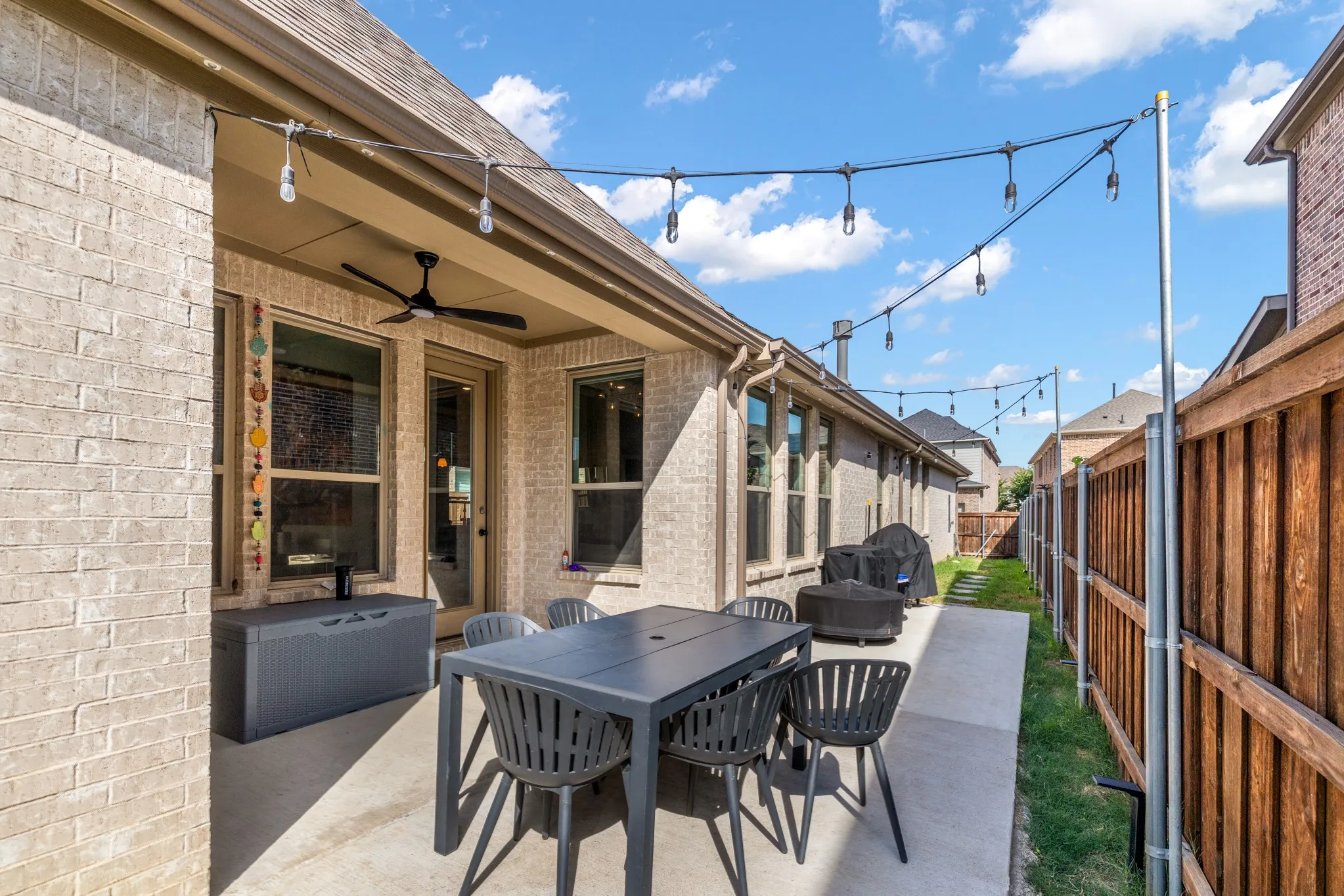 Modern covered patio featuring a concrete surface, black metal dining table with matching chairs, and overhead string lighting with pendant fixtures