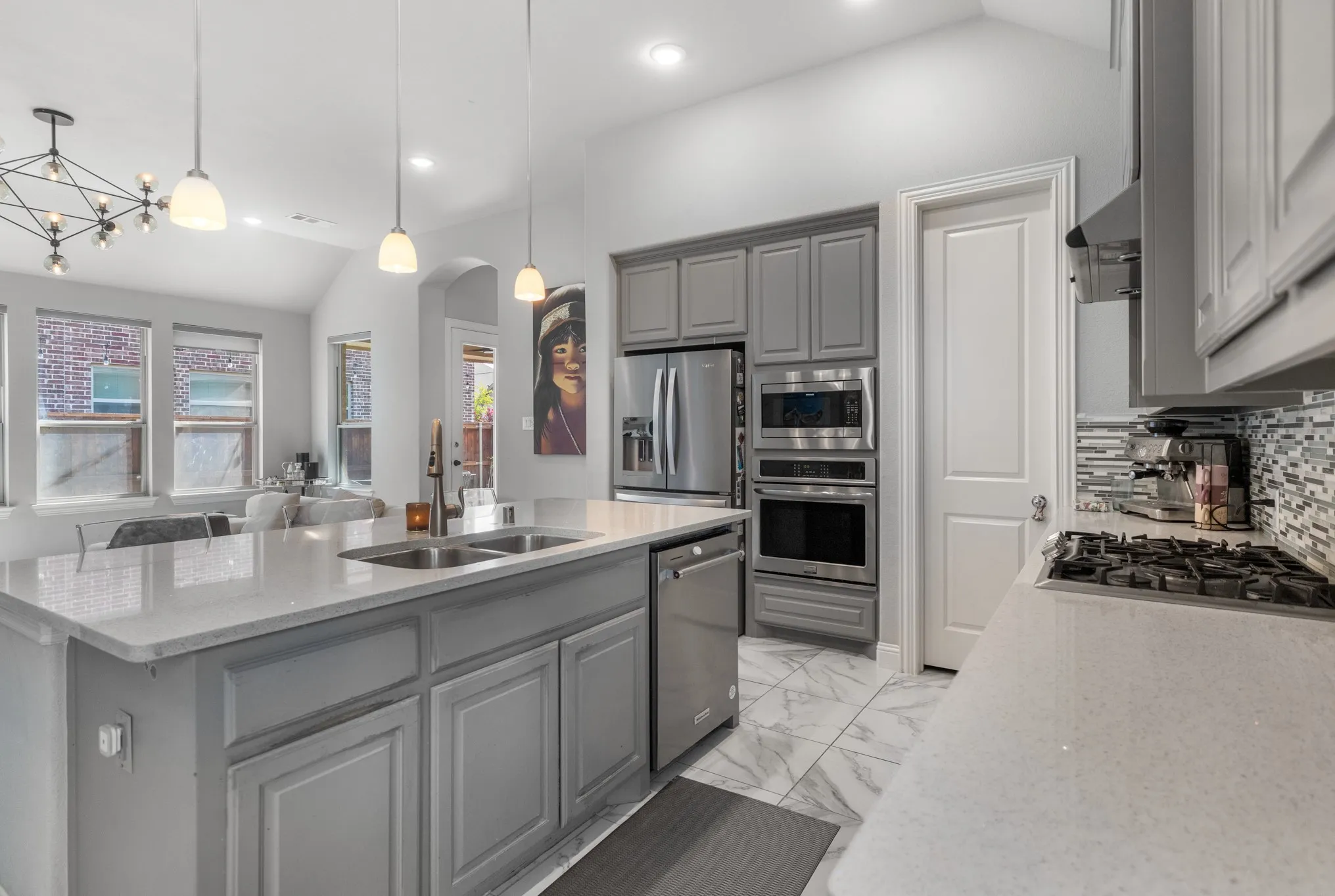 Spacious kitchen featuring an island with double sinks, stainless steel appliances, grey cabinetry, and a mosaic tile backsplash