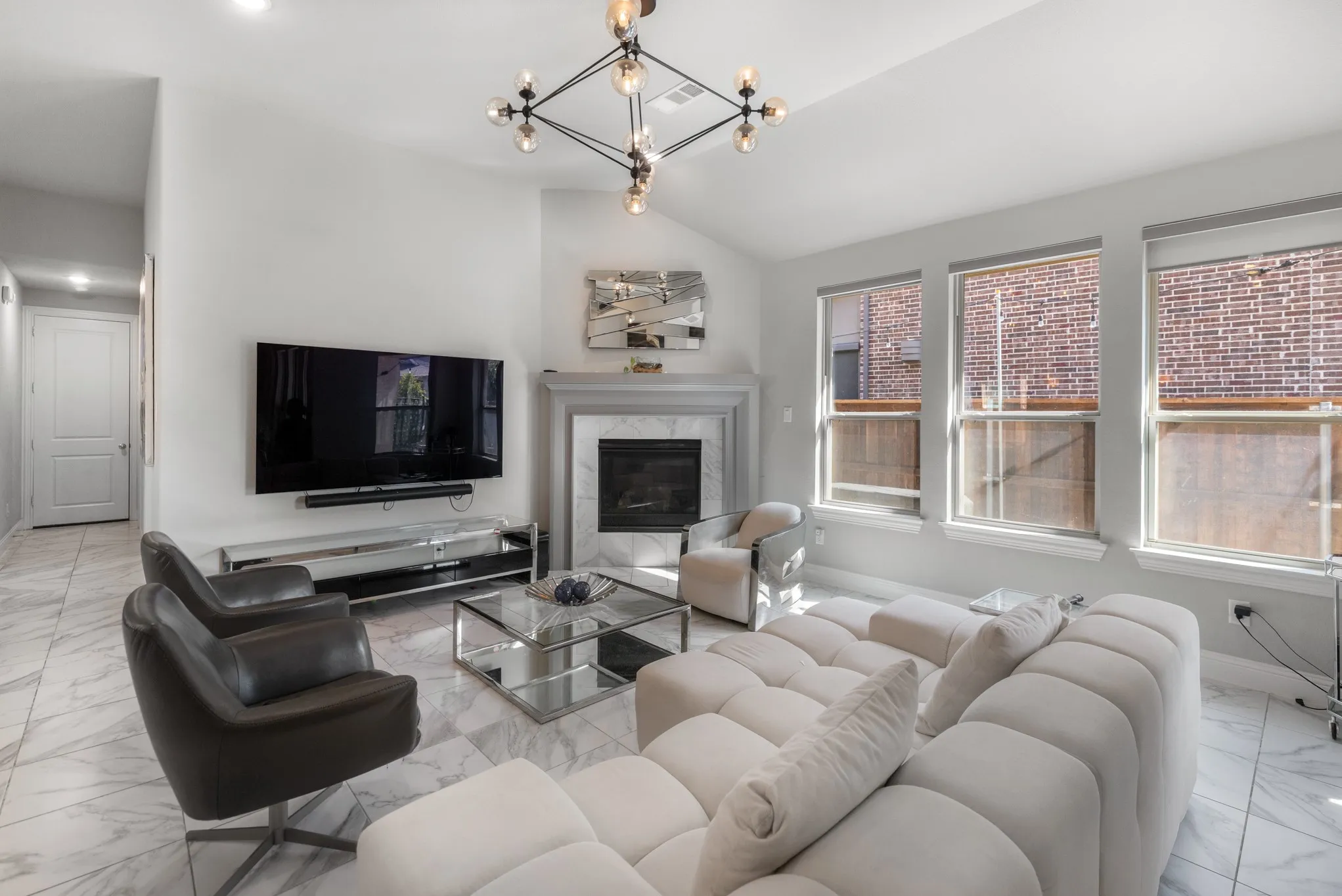Bright, open living room showcasing a curved sectional sofa, glass coffee table, and entertainment center with flat-screen television