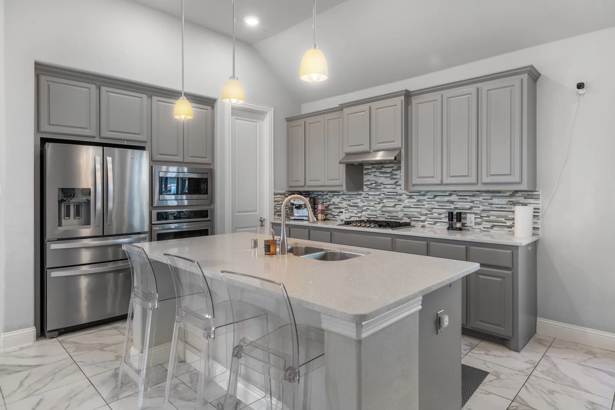 Sophisticated kitchen featuring custom gray cabinetry, stainless steel appliances including a French-door refrigerator and double wall ovens, quartz countertops, and a tile backsplash