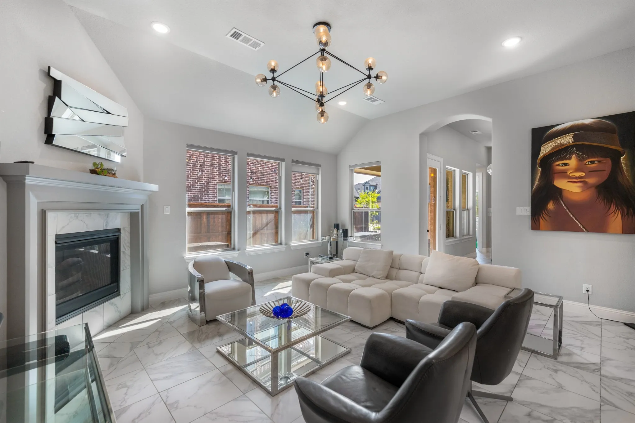 Living area featuring a fireplace with a stone surround, multiple windows, a high vaulted ceiling, recessed lighting, and a modern chandelier