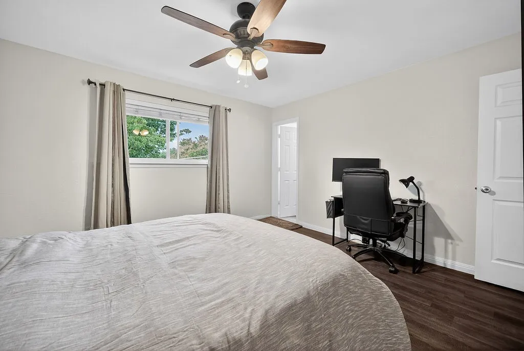 Bedroom with wood-finish flooring, light-colored walls, and a ceiling fan with integrated lighting