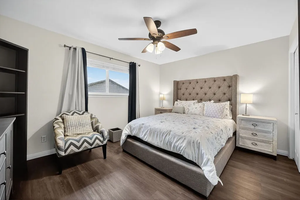 Spacious bedroom featuring wood-finish flooring, a ceiling fan with integrated lighting, and a window with blinds