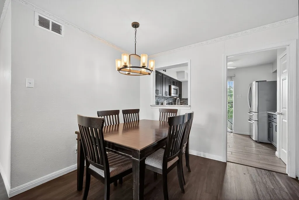 Dining area with wood-finish flooring, a contemporary chandelier, crown molding, and a pass-through window to the kitchen