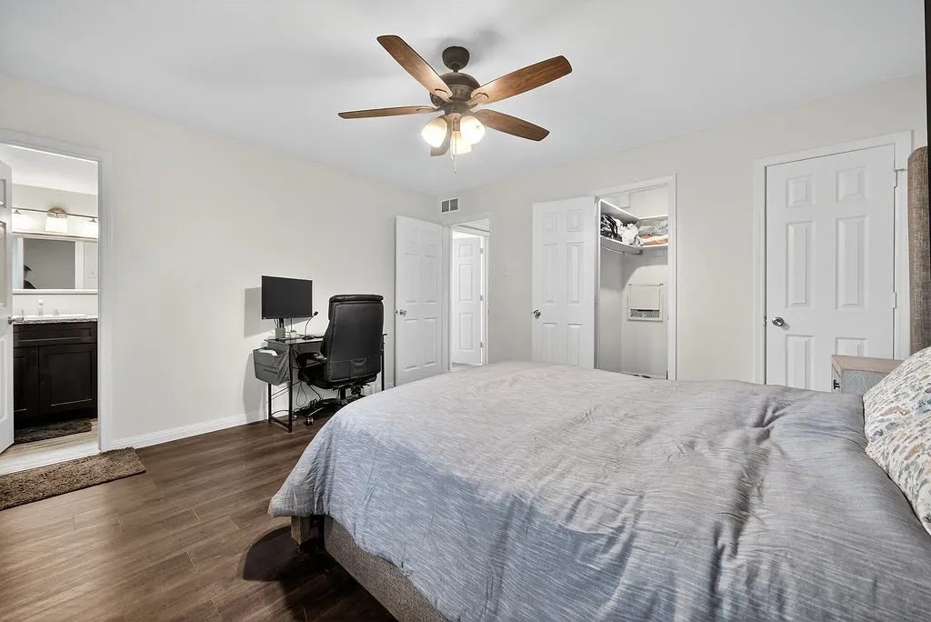 Spacious room featuring wood-finish flooring, light-colored walls, a ceiling fan with integrated lighting, and multiple white panel doors