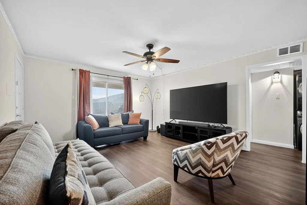 Living area featuring wood-finish flooring, a ceiling fan with integrated lighting, and crown molding