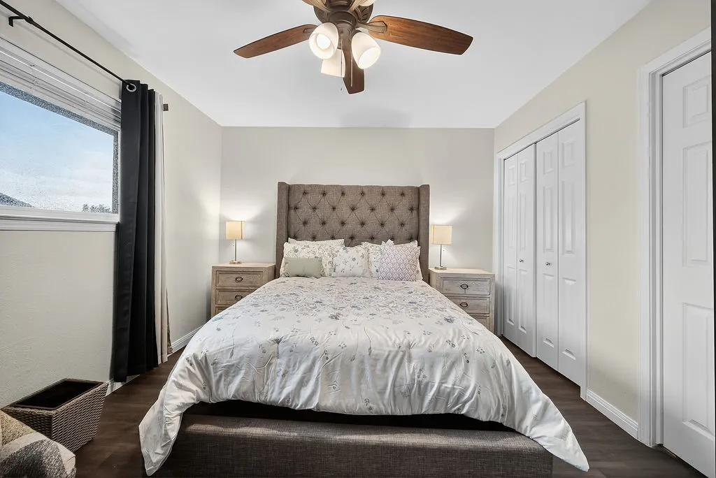 Bedroom featuring wood-finish flooring, a ceiling fan with integrated lighting, a window with window treatments, and white bi-fold closet doors