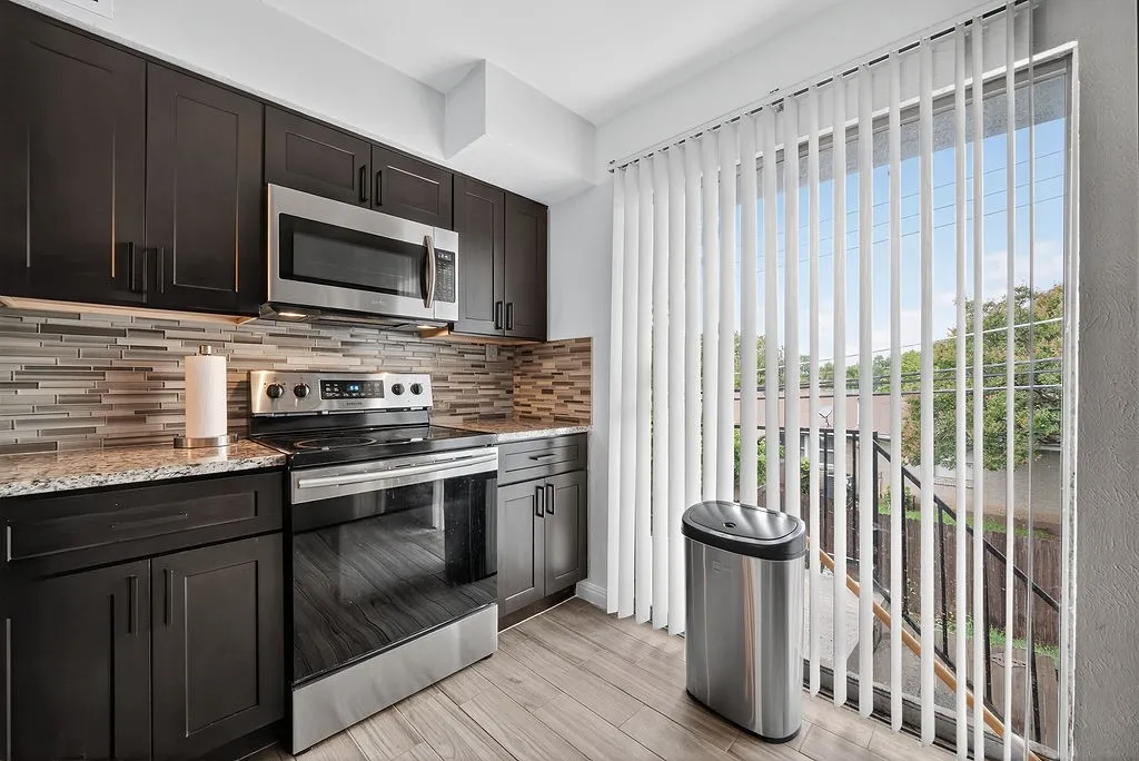 Kitchen with dark wood cabinetry, stainless steel appliances, granite countertops, and a mosaic tile backsplash