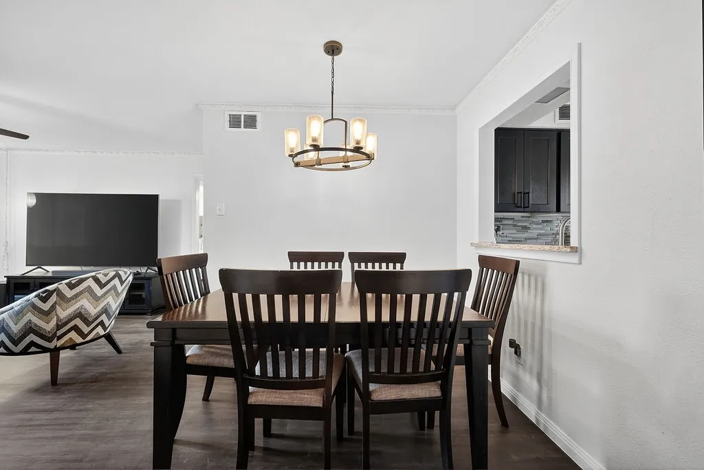 Dining area featuring wood-finish flooring, a modern chandelier, and a pass-through window with a granite-look counter