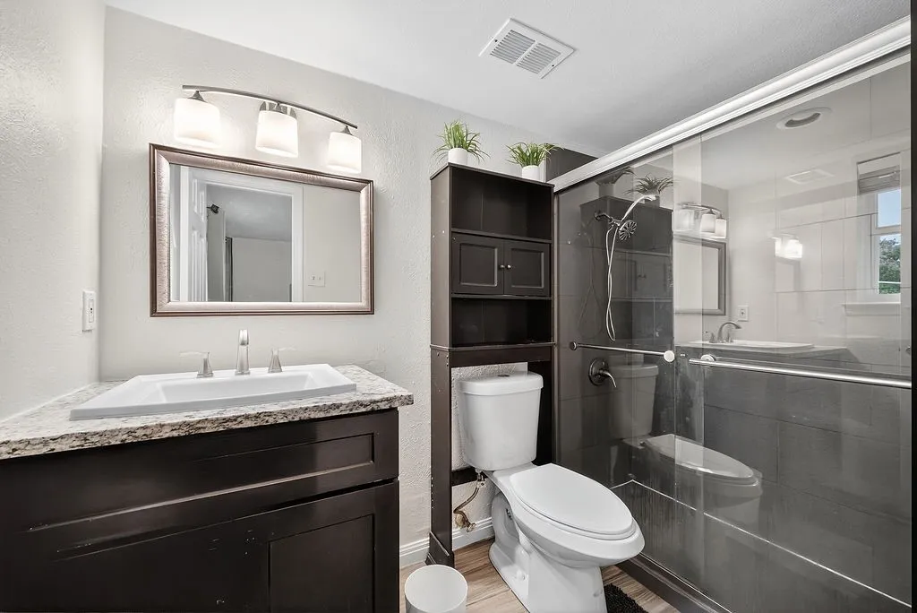 Modern bathroom featuring a dark wood-finish vanity with a white rectangular sink, a granite-finish countertop, and a framed mirror