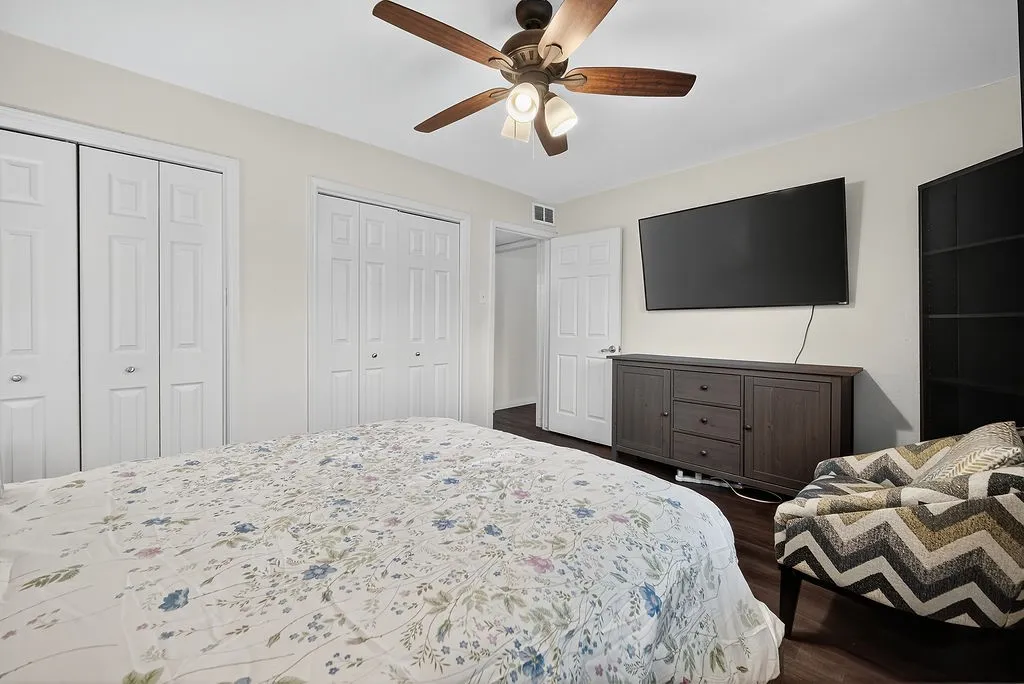 Spacious room featuring two sets of bi-fold closet doors, wood-finish flooring, a ceiling fan with integrated lighting, and a solid-core entry door
