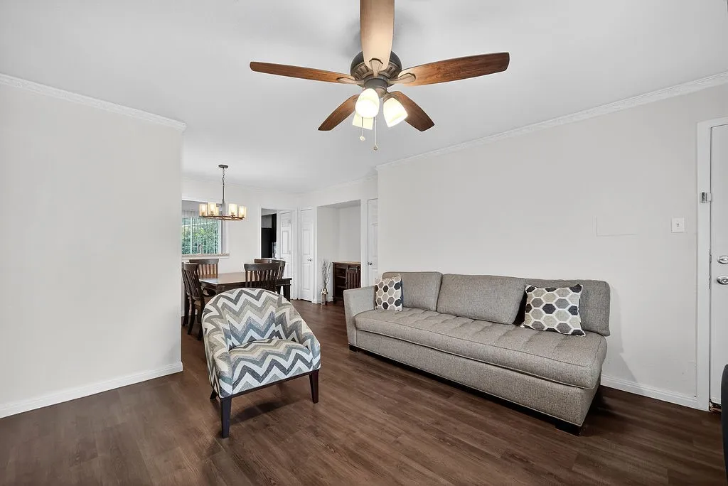 Living area featuring wood-finish flooring, a ceiling fan with integrated lighting, and crown molding