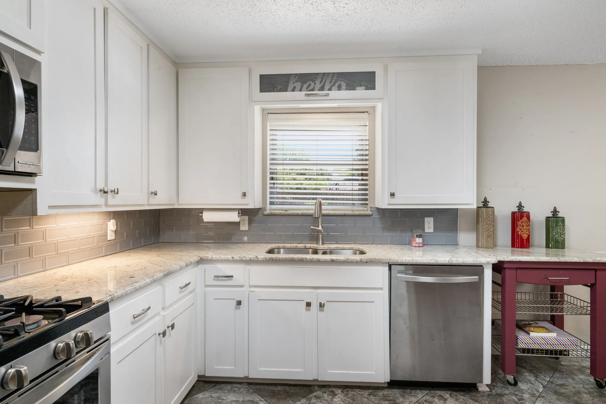 Updated kitchen featuring white cabinetry, stainless steel appliances including a gas range and dishwasher, ceramic tile backsplash, and laminate countertops with an undermount sink