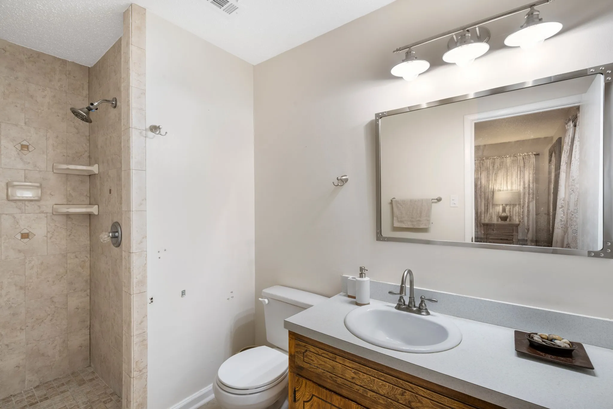 Spa-inspired bathroom featuring a curved white porcelain sink with brushed nickel faucet, marble-look tile shower surround with frameless glass enclosure, wood-finish vanity cabinetry, and dual recessed ceiling lights