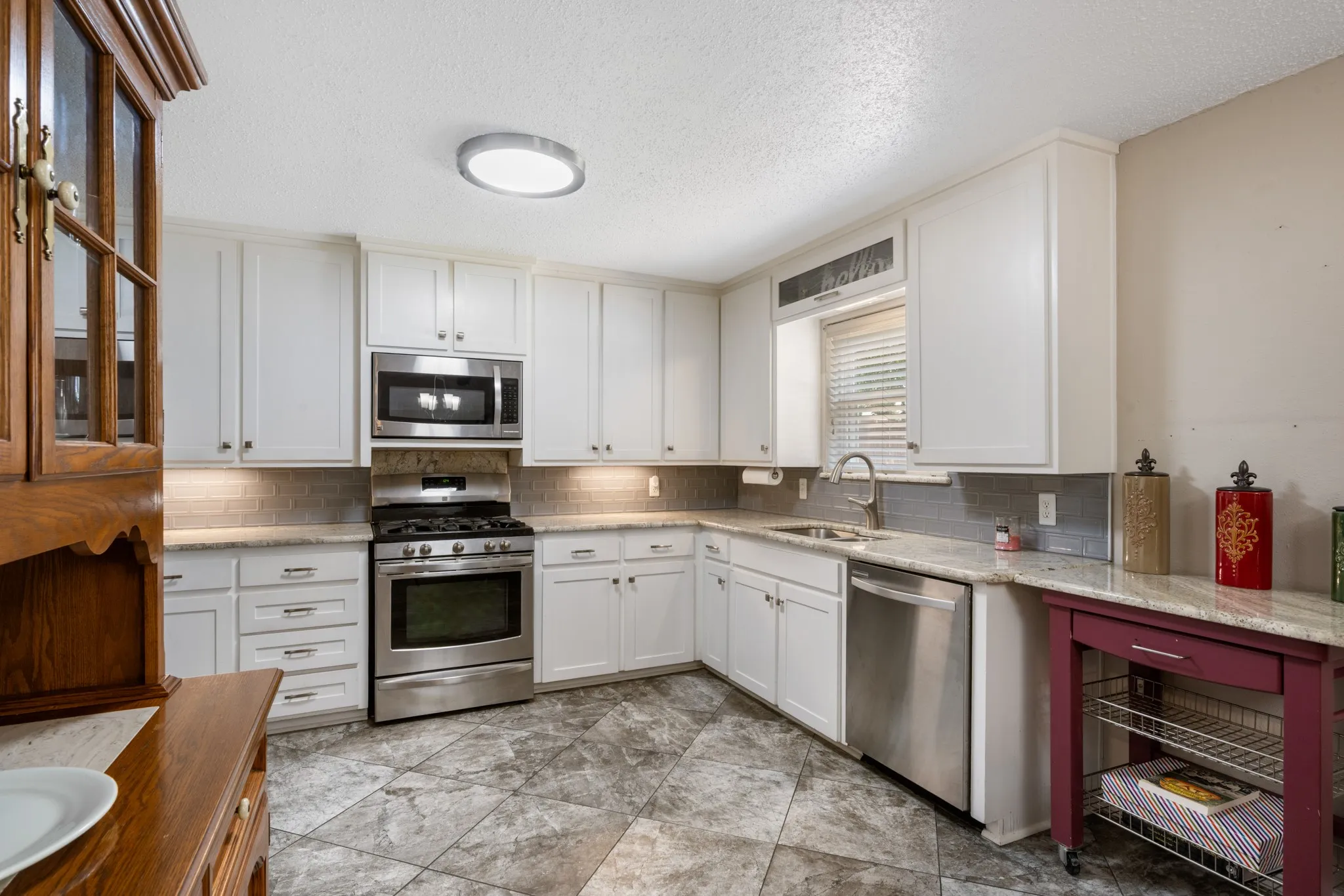 Kitchen featuring white cabinetry, stainless steel appliances, light-toned countertops, tile flooring, and under-cabinet lighting